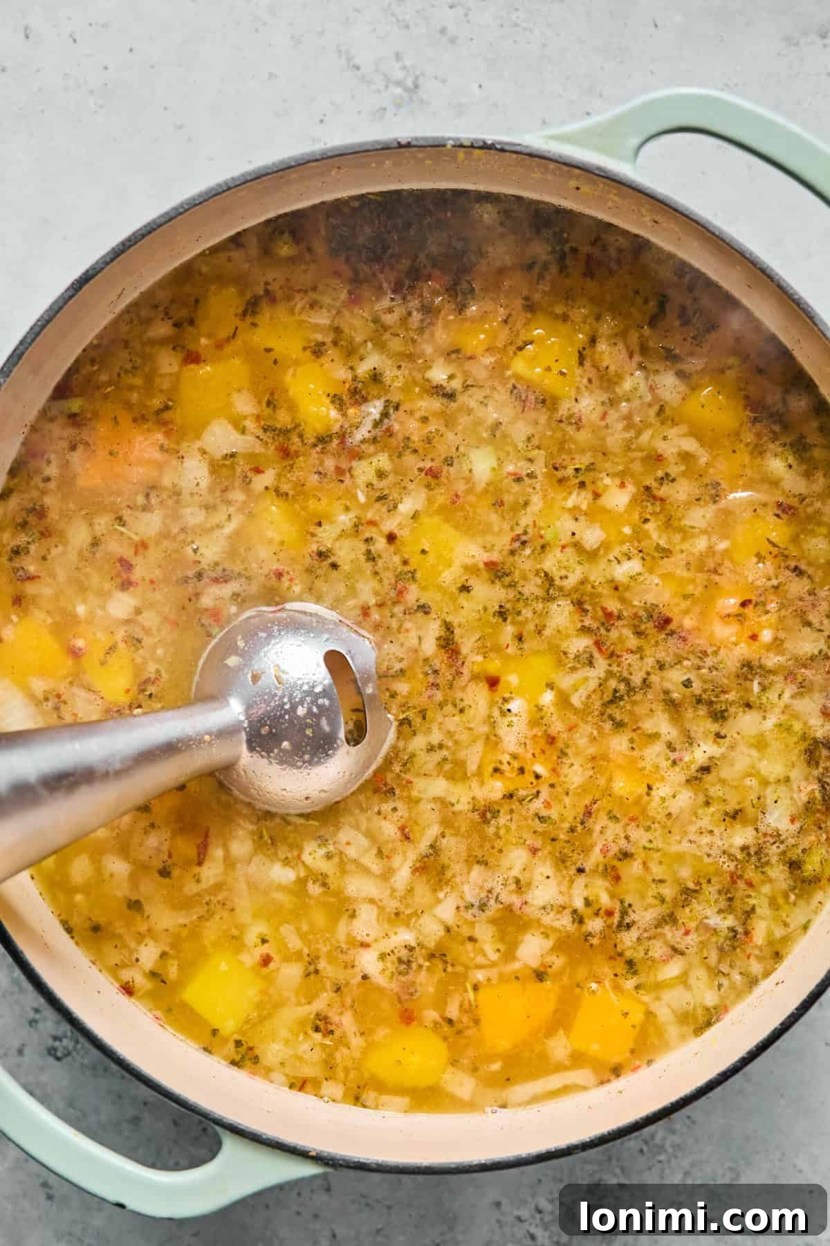 Immersion blending creamy butternut squash soup base before adding noodles.