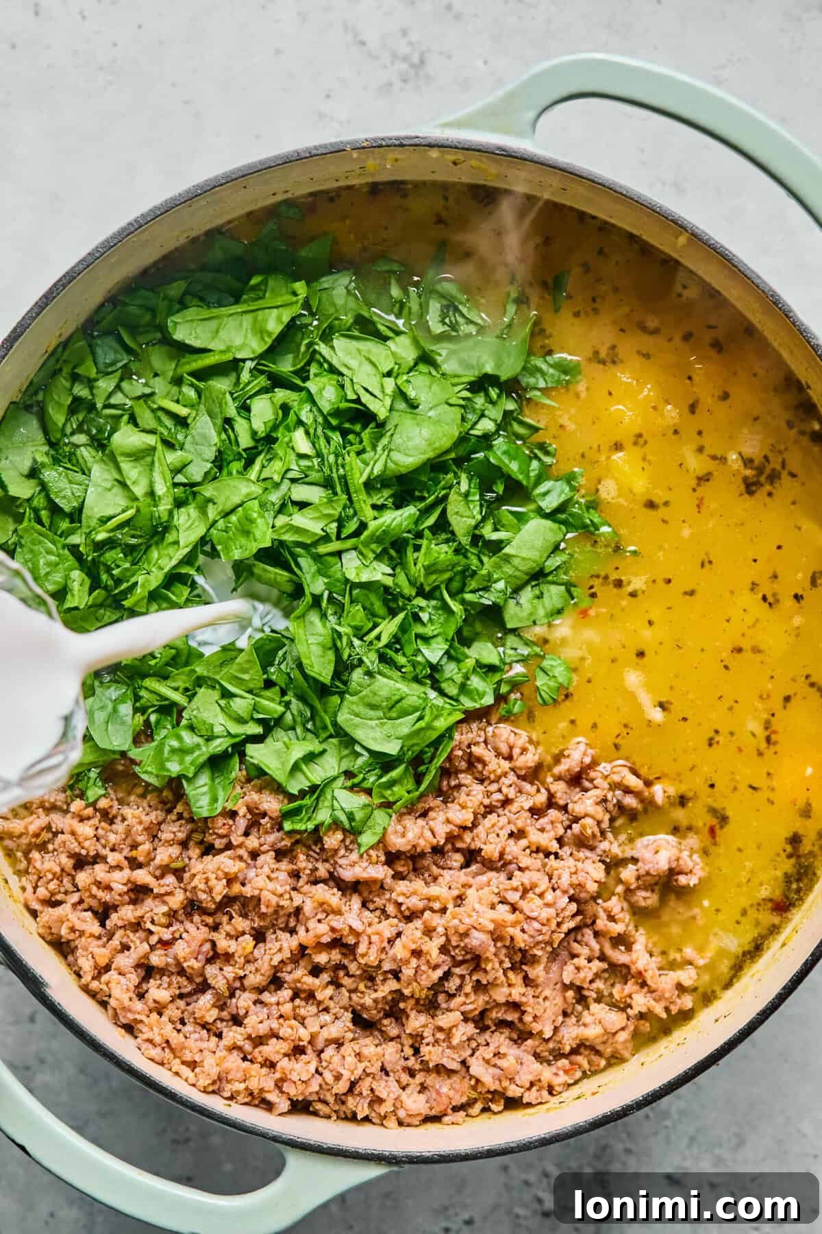 Stirring sausage, spinach, and half-and-half into the creamy lasagna soup mixture.