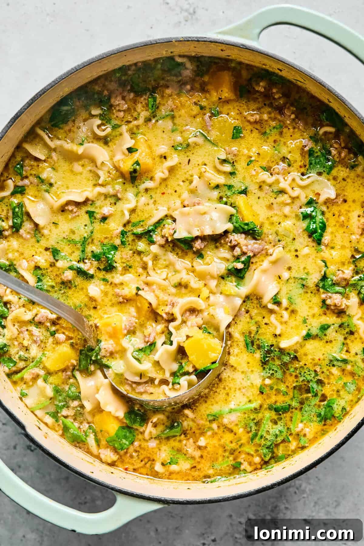 Butternut squash lasagna soup in a large pot with a ladle ready to pour into a bowl.