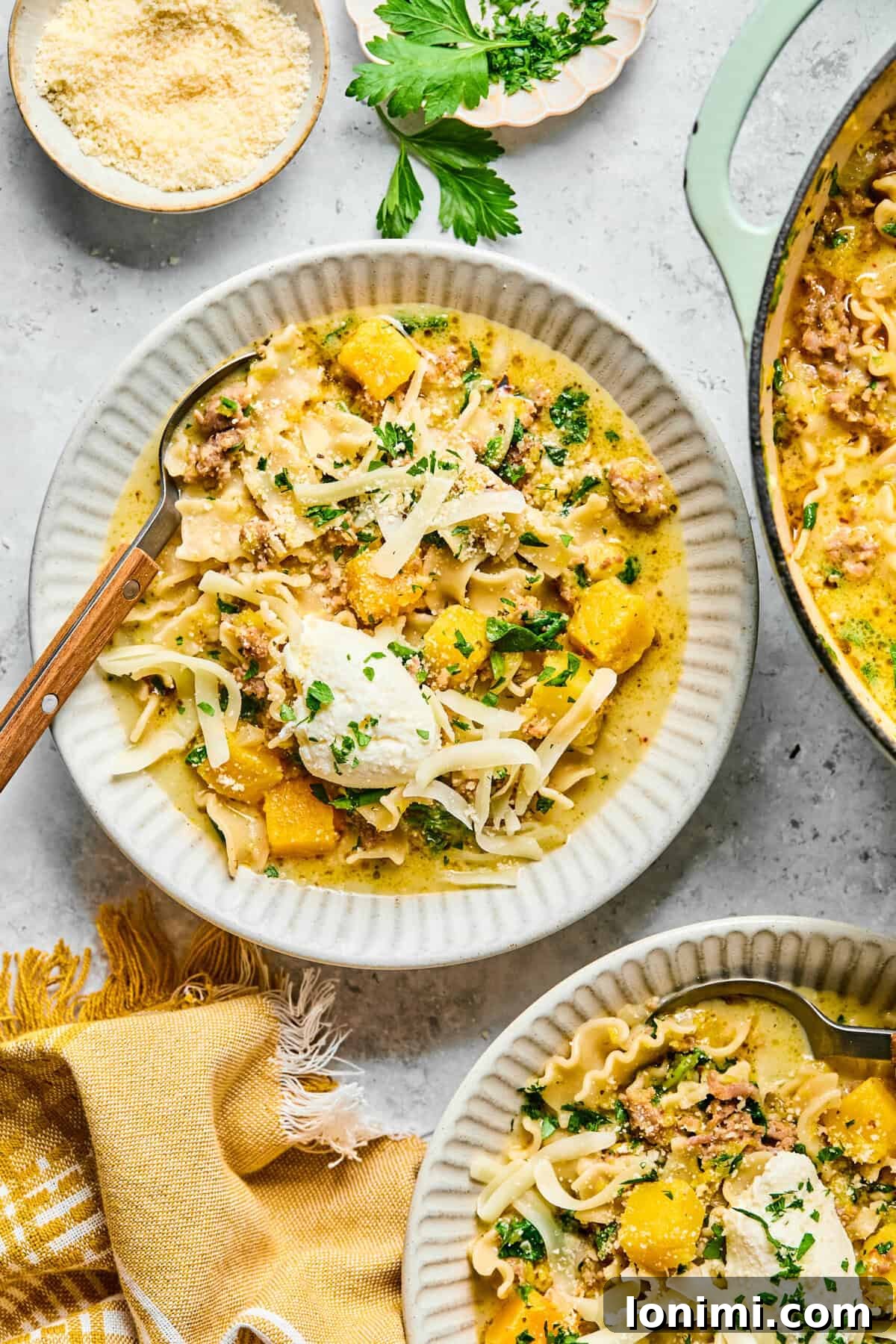 Close-up of a hearty bowl of butternut squash lasagna soup with noodles, sausage, and melted cheese.