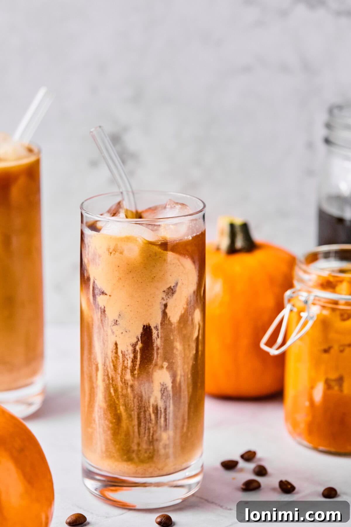 Homemade Protein Pumpkin Cold Foam Perfection 2 A refreshing glass of cold brew topped with a rich, creamy pumpkin protein cold foam, surrounded by decorative miniature pumpkins, evoking a cozy autumn vibe.