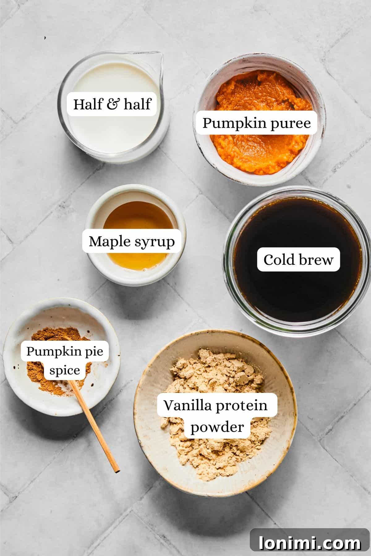 Homemade Protein Pumpkin Cold Foam Perfection 3 A collection of ingredients for homemade protein cold foam, including cold brew, vanilla protein powder, pumpkin puree, pumpkin pie spice, half and half, and maple syrup, artfully arranged in nesting bowls.