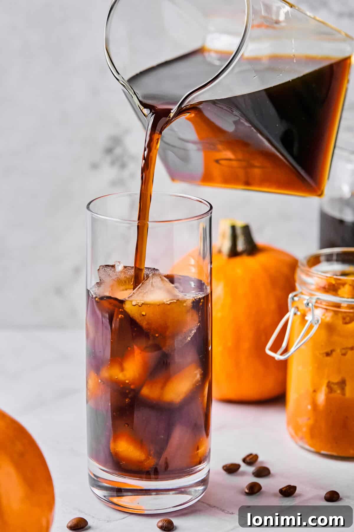 Homemade Protein Pumpkin Cold Foam Perfection 6 A stream of cold brew coffee being poured into a clear glass filled with ice, preparing the base for the pumpkin cold foam.