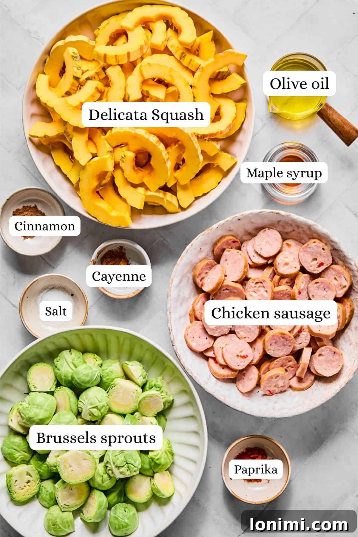 ingredients for a harvest sheet pan dinner in nesting bowls, including delicata squash, chicken sausage, Brussels sprouts, olive oil, maple syrup, and spices