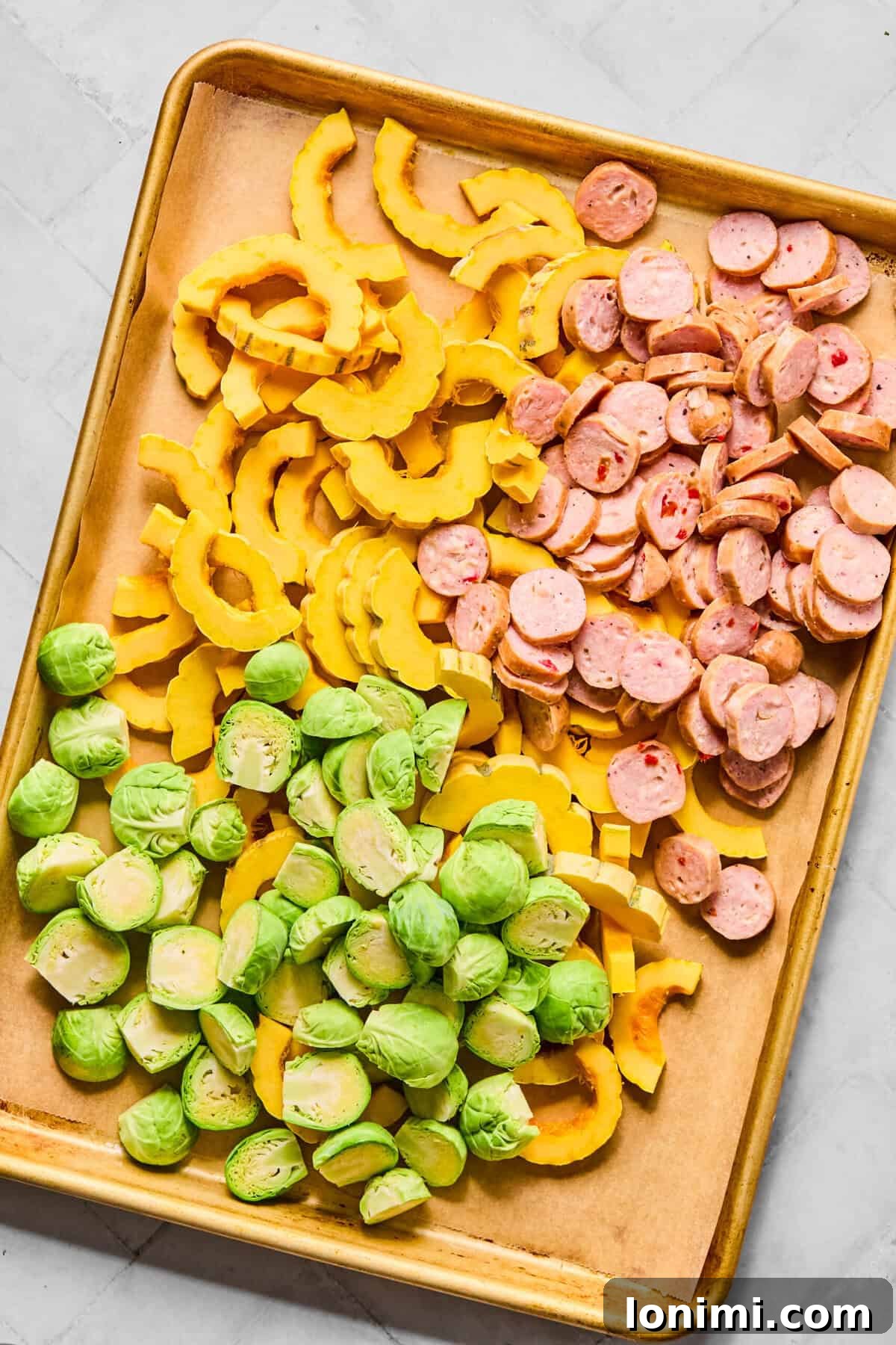 a sheet pan with uncooked delicata squash, chicken sausage, and brussels sprouts, ready for roasting