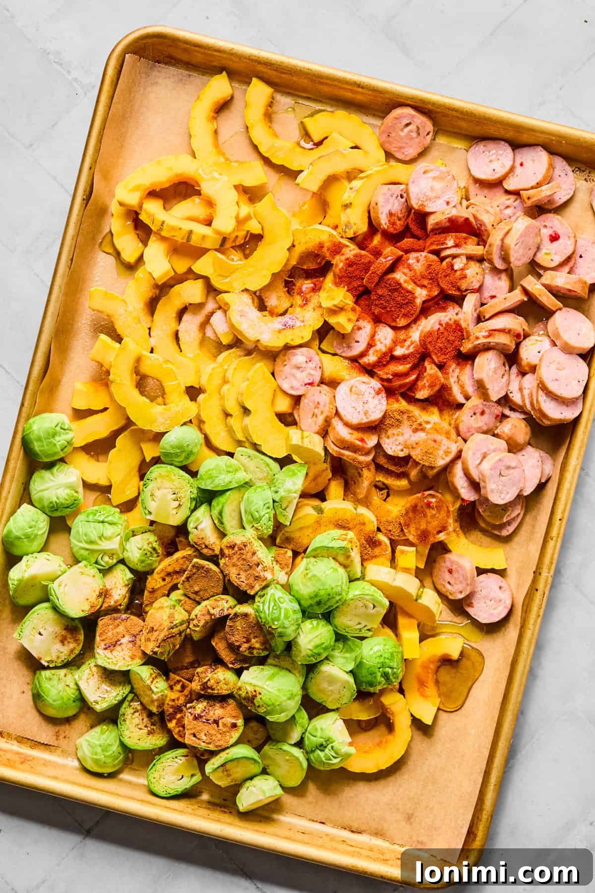 a sheet pan with sausage, squash, and Brussels sprouts drizzled with olive oil and maple syrup, and seasoned with spices