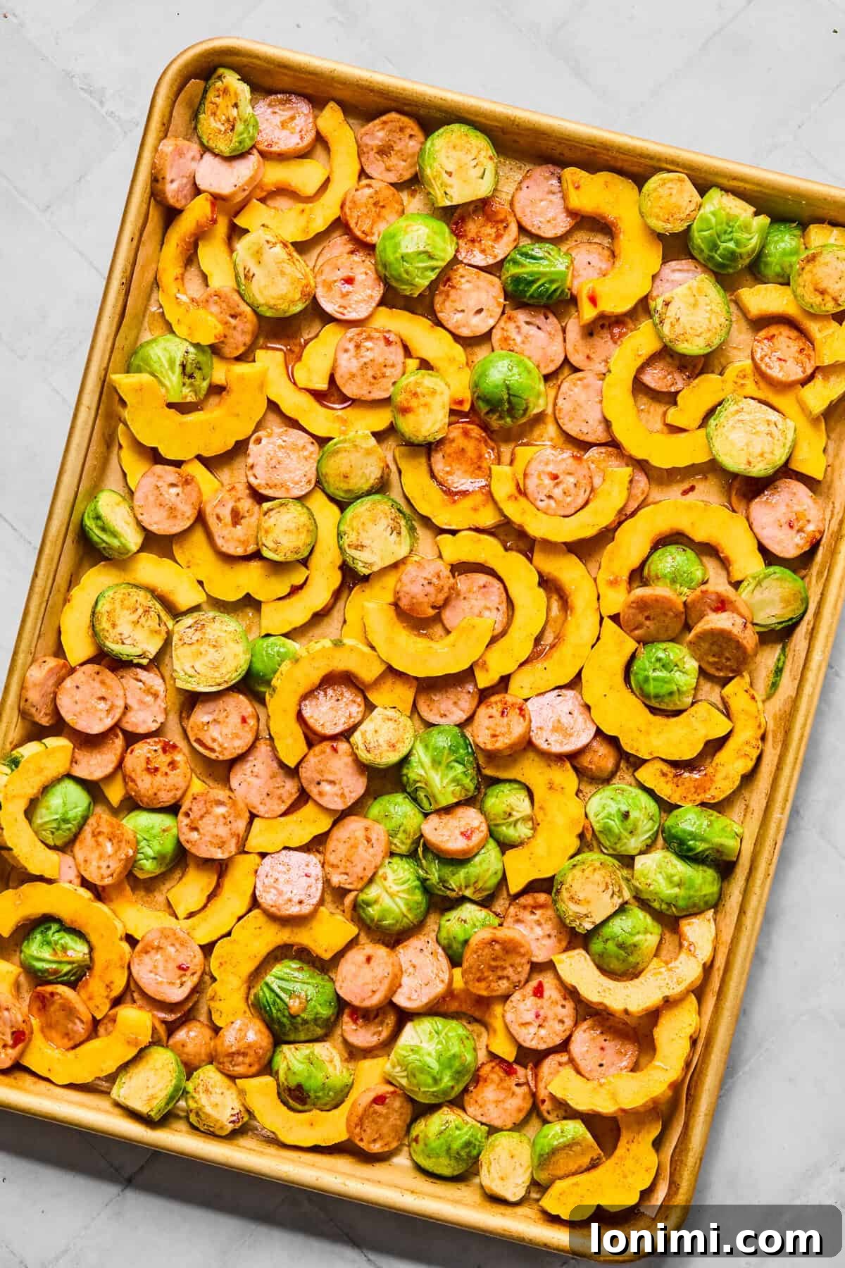vegetables and sausage mixed on a sheet pan, spread out in a single layer for roasting