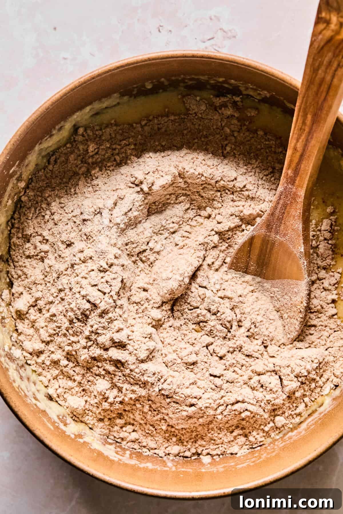 Wholesome Apple Cinnamon Protein Muffins Gluten Free 6 The dry ingredients are gently folded into the wet mixture within a large mixing bowl, creating a harmonious batter for the muffins.