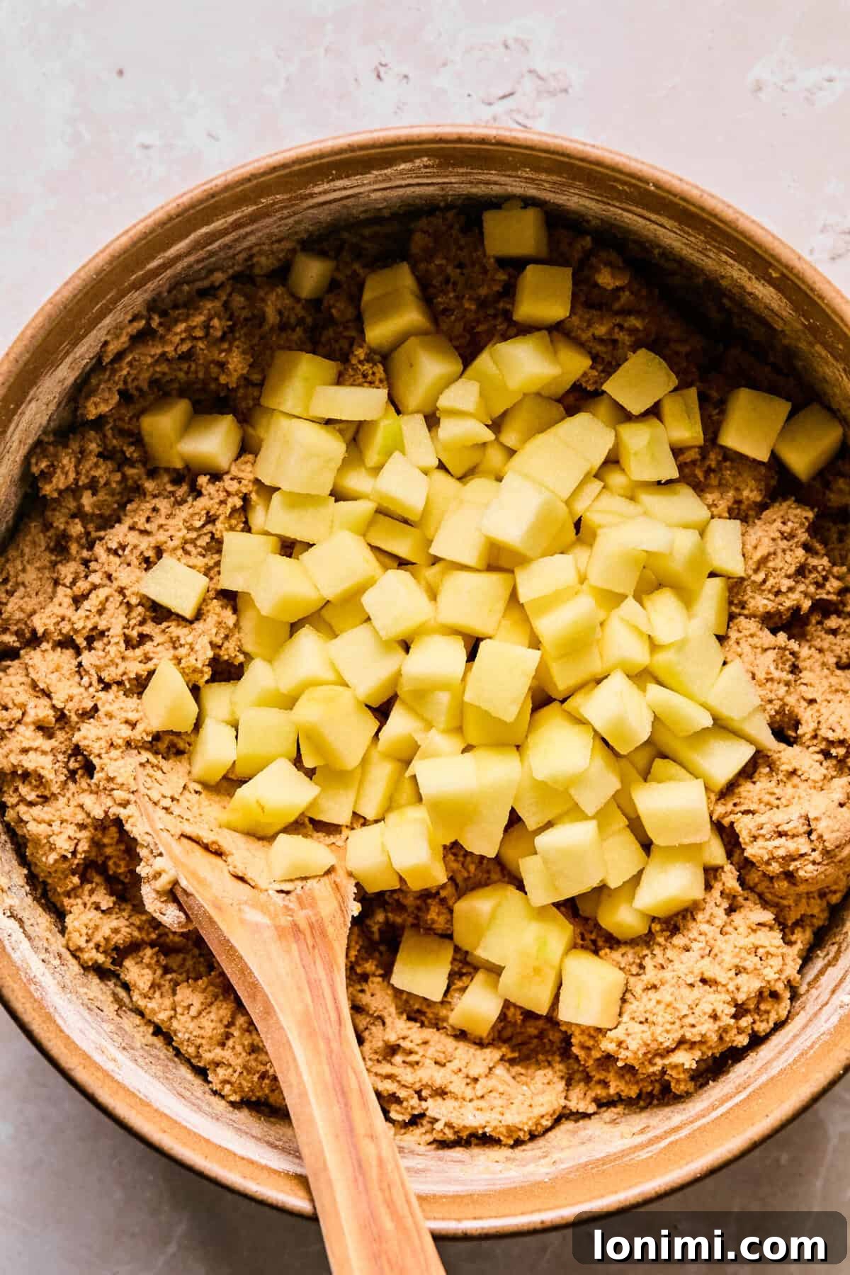 Wholesome Apple Cinnamon Protein Muffins Gluten Free 7 Finely diced apples are carefully folded into the apple cinnamon protein muffin dough using a sturdy wooden spoon, ensuring even distribution throughout the batter.