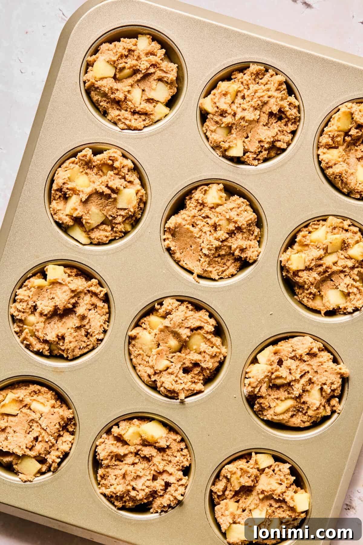 Wholesome Apple Cinnamon Protein Muffins Gluten Free 8 The apple cinnamon protein muffin batter is evenly divided among the 12 cups of a muffin tin, filled nearly to the top, promising generously sized baked goods.