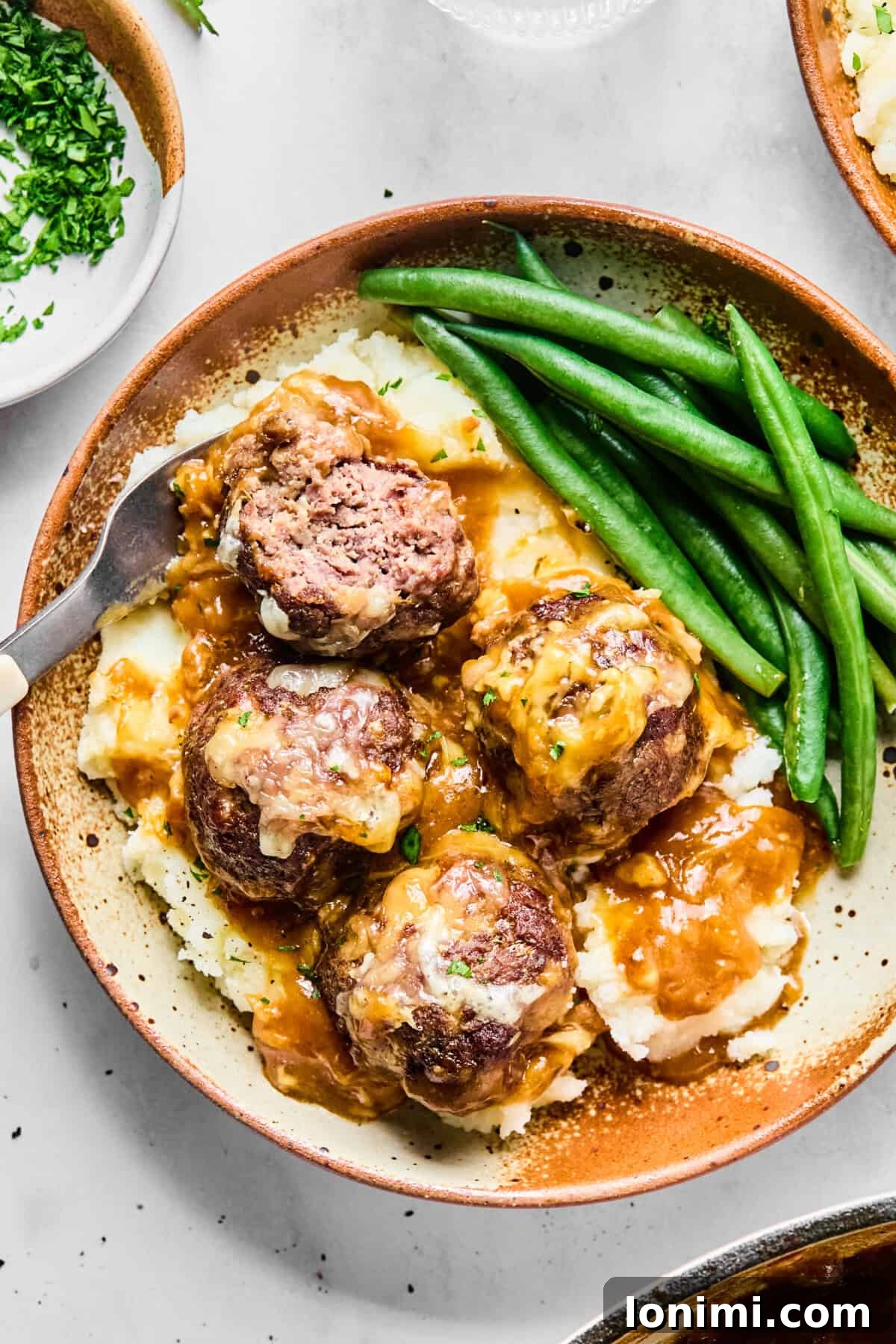 Baked French onion meatballs with rich onion gravy and melted Gruyère cheese, ready to serve.