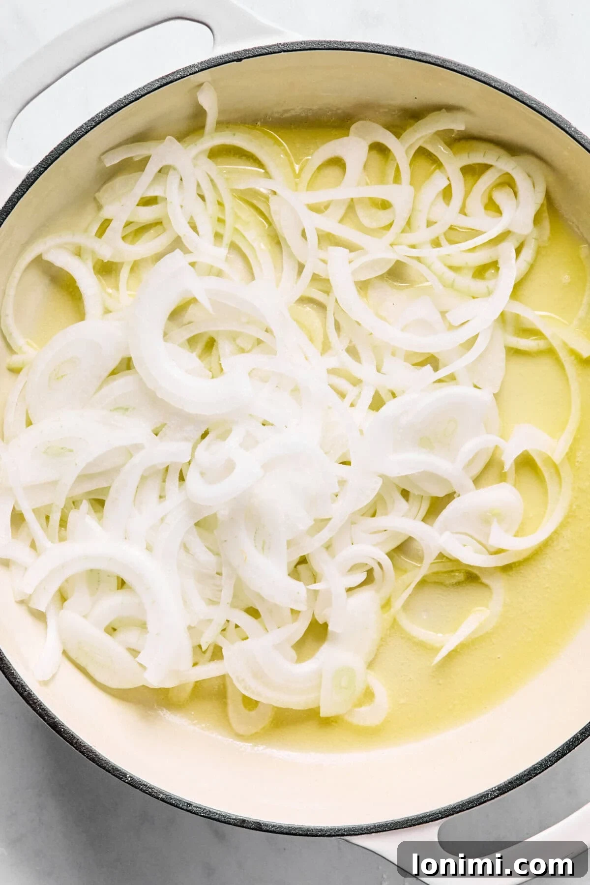 Large oven-safe skillet with melted butter and sliced onions.