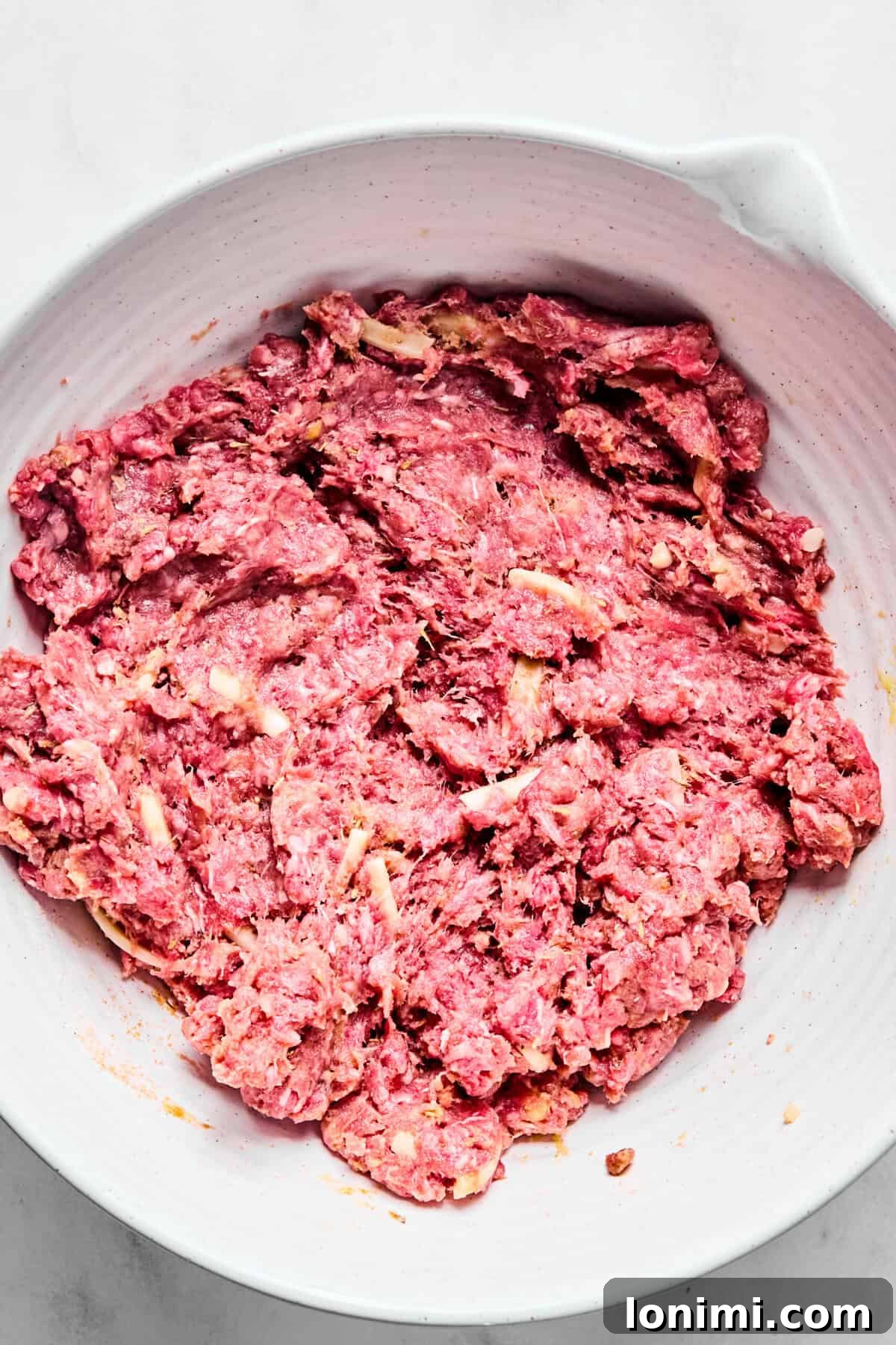 Ground beef, gluten-free flour, egg, seasonings, Worcestershire sauce, and shredded cheese mixed in a white bowl.
