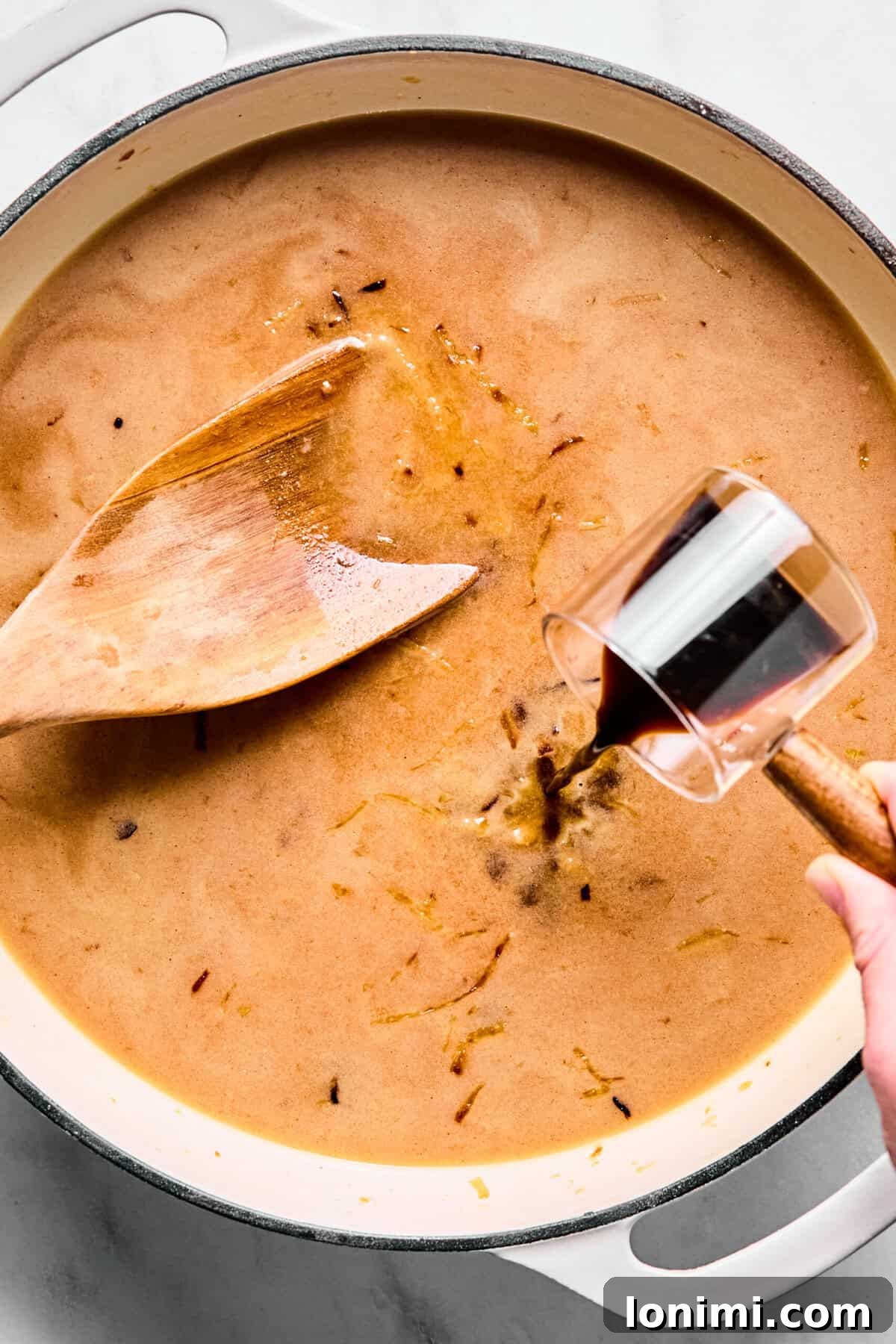 Beef broth, Worcestershire sauce, thyme, and salt being poured into the oven-safe skillet over the caramelized onions.