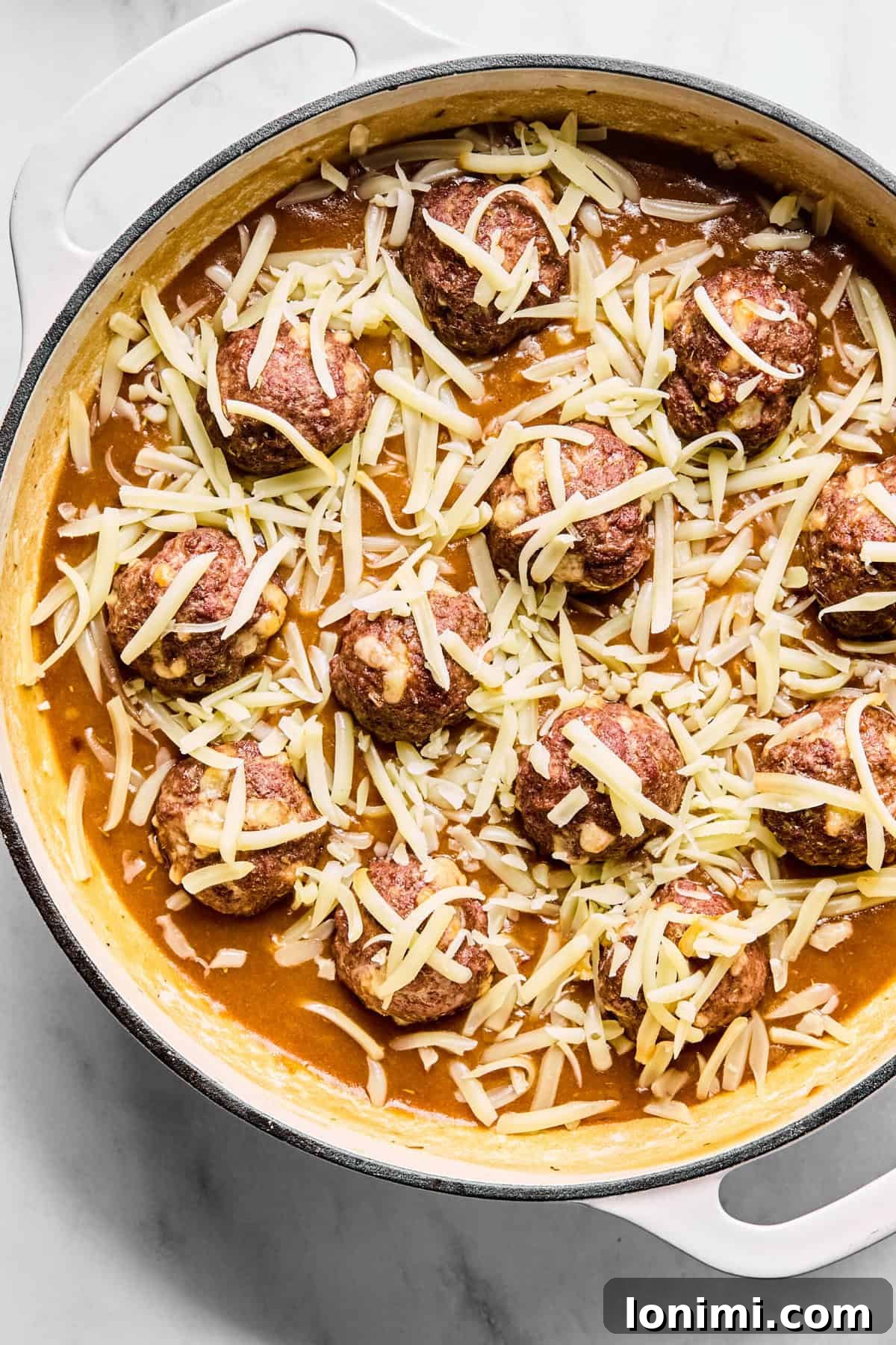 Cooked meatballs nestled into the large oven-safe skillet with onion gravy and shredded cheese covering them.