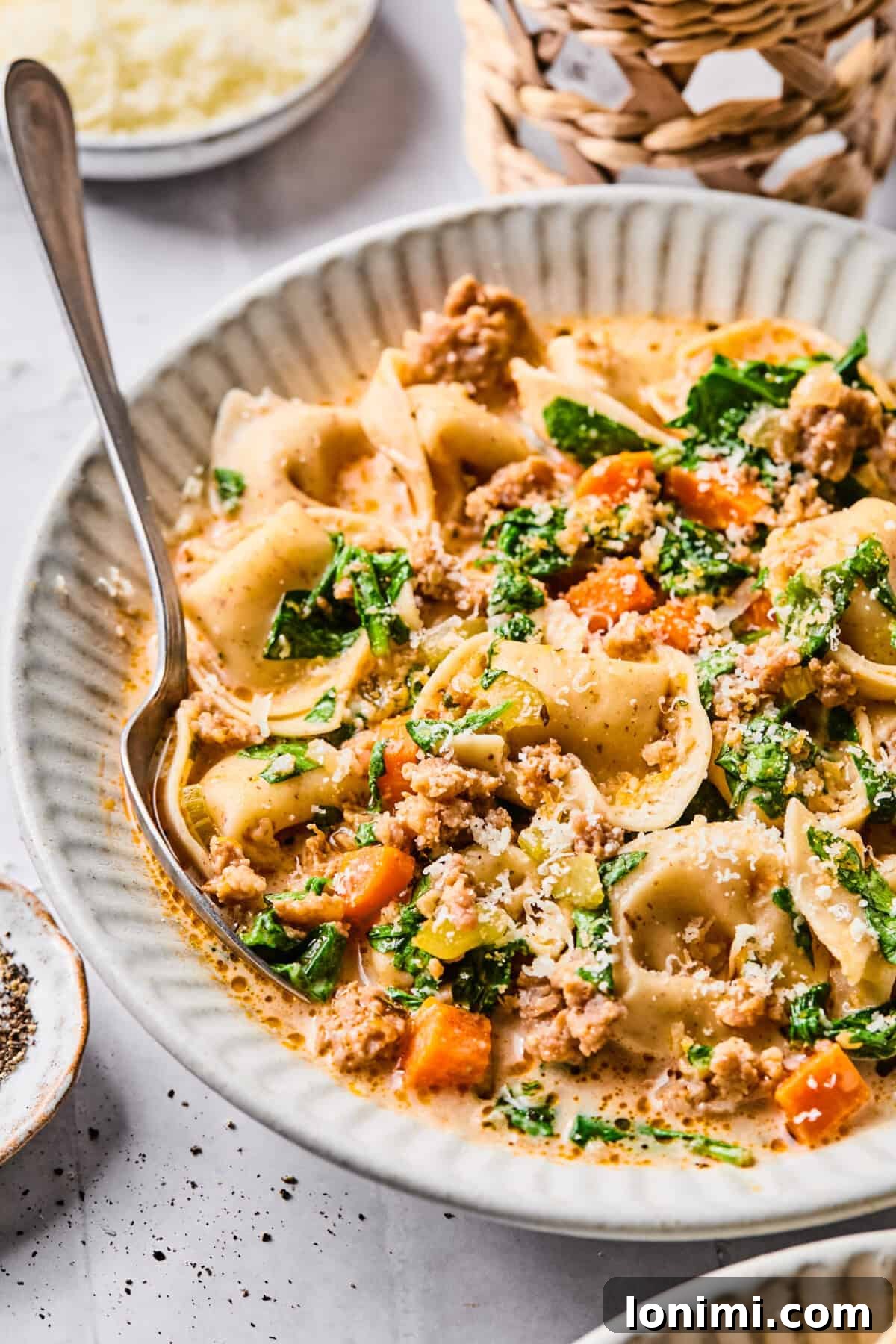 Slow Cooker Creamy Sausage Tortellini Soup 12 a close up of sausage tortellini soup with veggies, spinach and parmesan cheese on top.