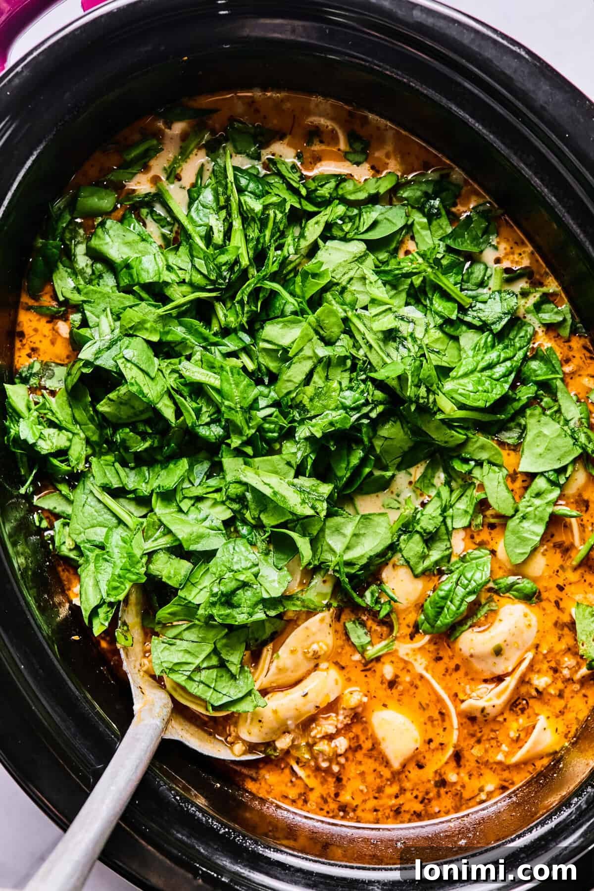 Slow Cooker Creamy Sausage Tortellini Soup 10 adding raw spinach to the crockpot soup.