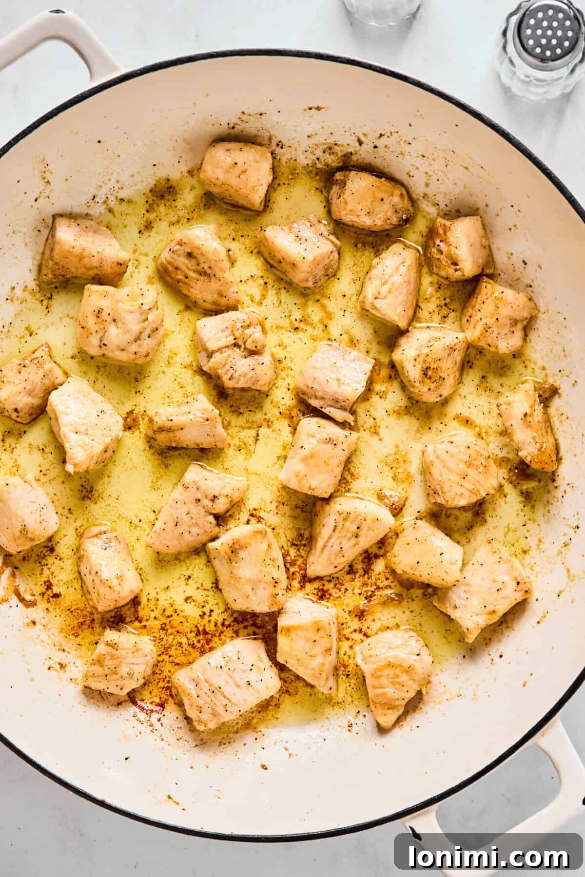 Chicken pieces browning in olive oil in a large sauté pan.