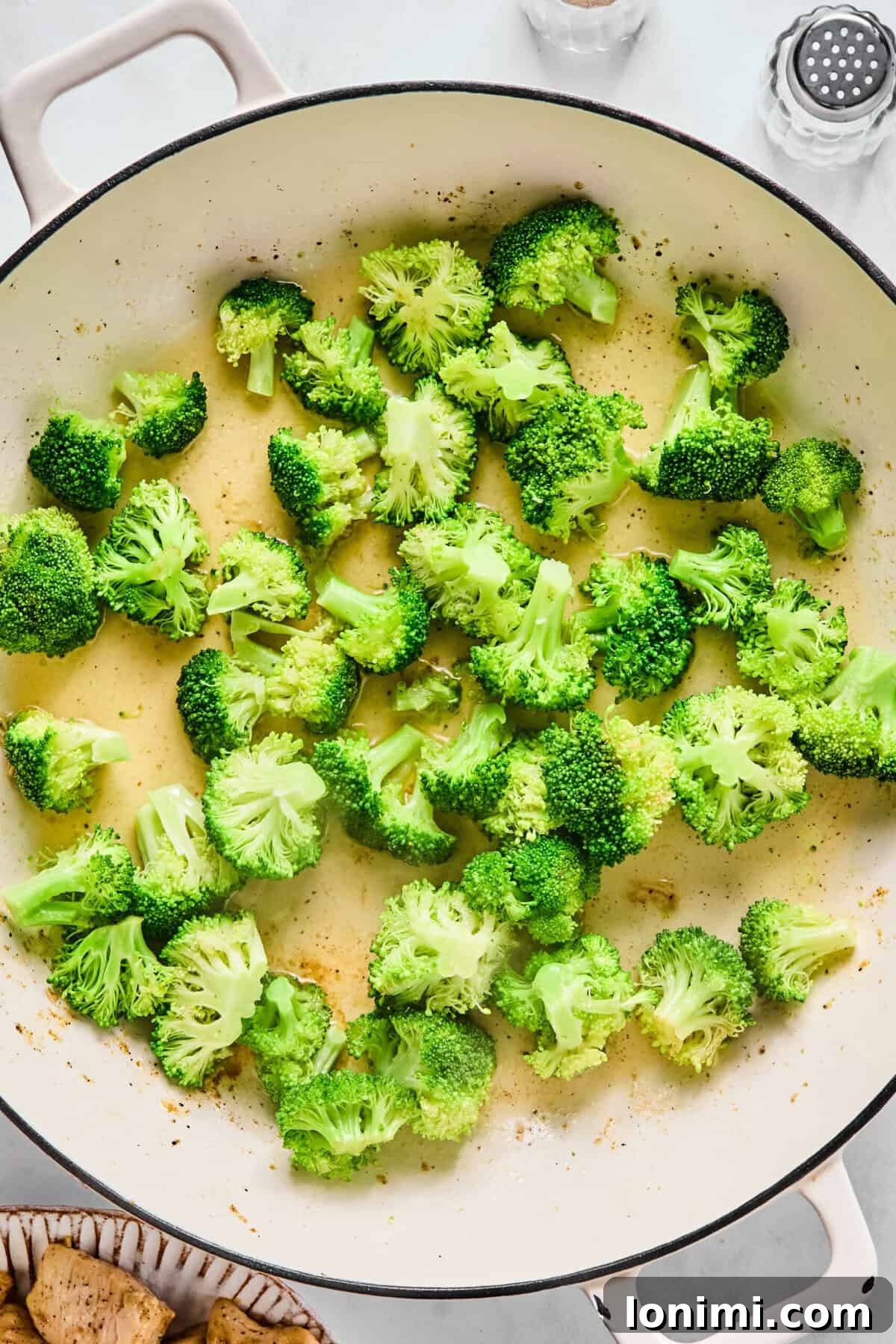 Broccoli florets steaming with a splash of water in a large sauté pan.
