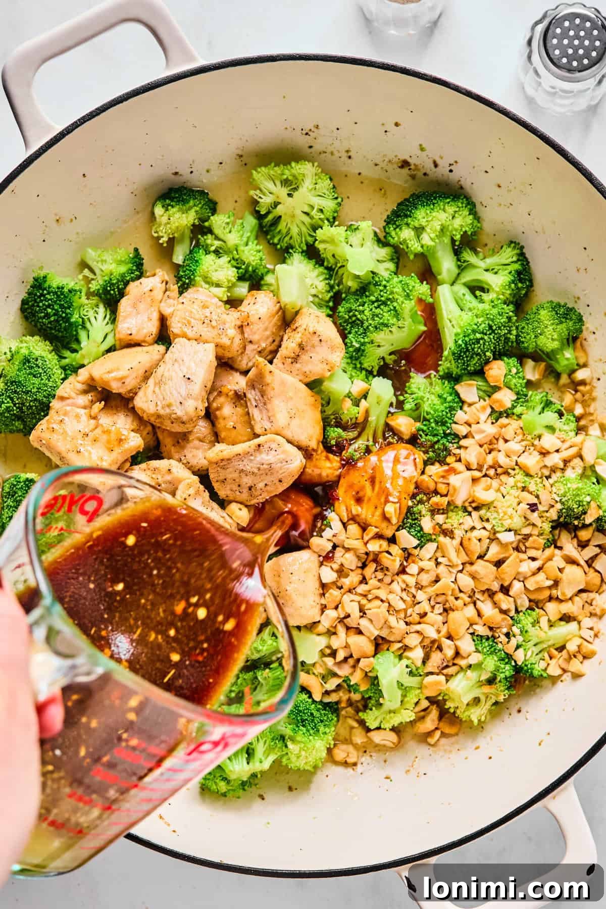 Chicken and cashews added back to large sauté pan with broccoli; stir fry sauce is being poured in.
