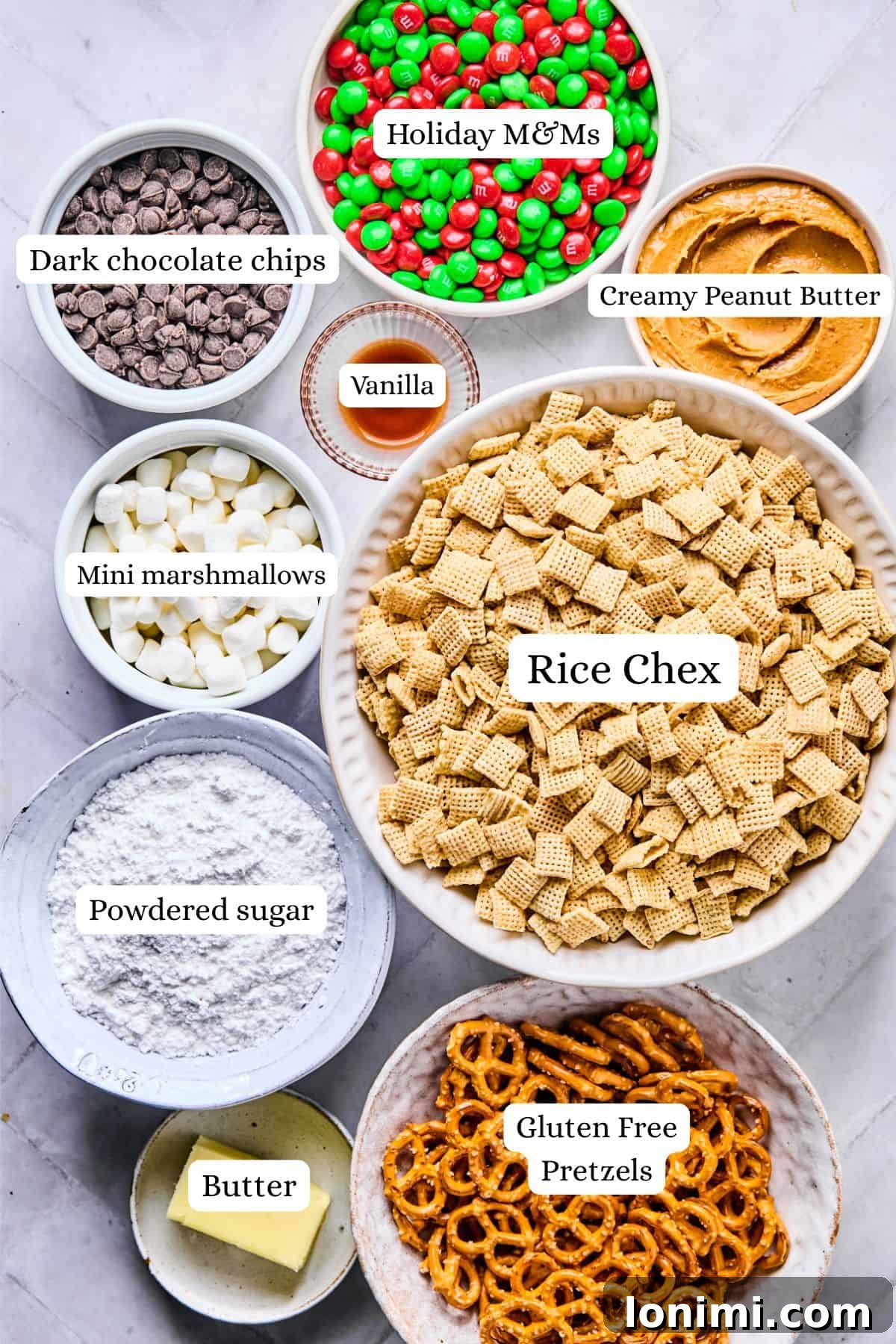 Christmas puppy chow ingredients labeled and laid out in bowls including rice chex, powdered sugar, pretzels, peanut butter, vanilla, and chocolate chips on a white background.