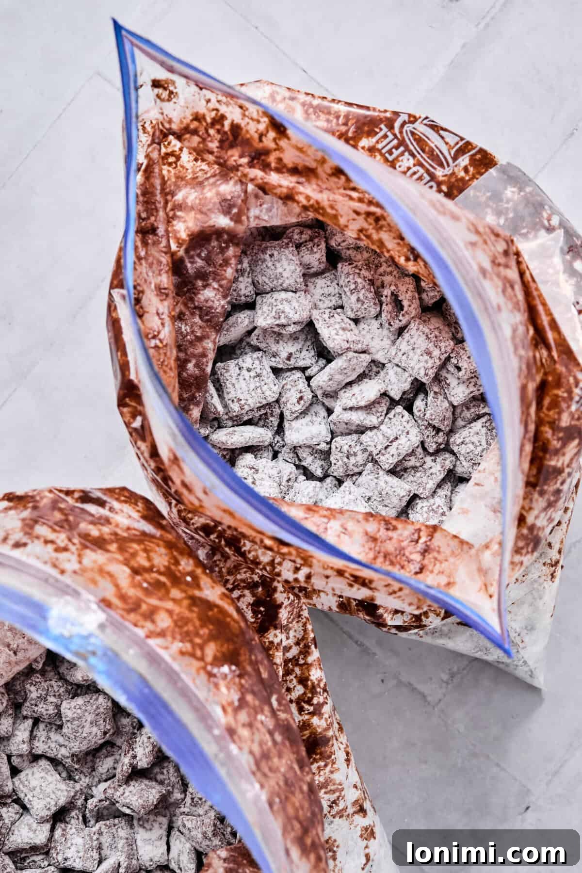 Chocolate-coated cereal divided between two gallon-sized zip-top bags and shaken vigorously with powdered sugar until fully coated in a snowy white layer.