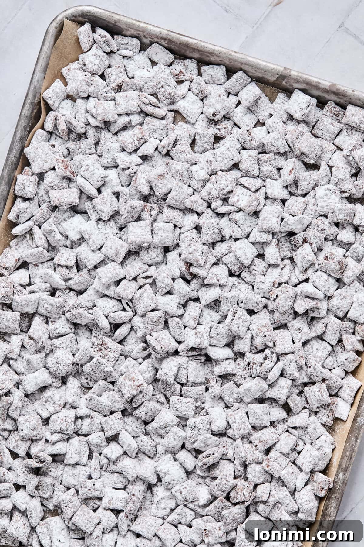 The powdered sugar-coated cereal mixture spread out evenly onto a parchment-lined baking sheet, allowing it to cool and set.