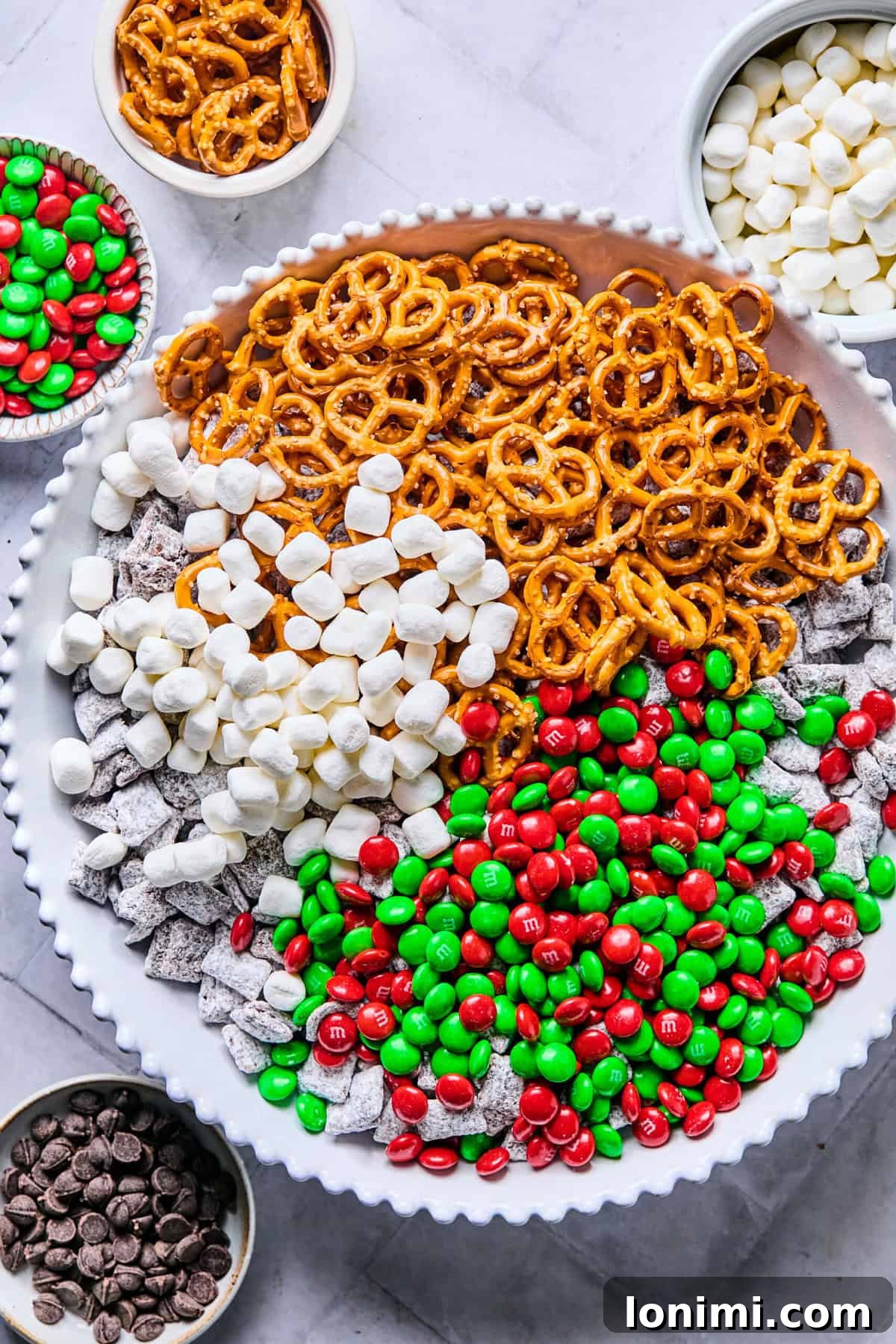The cooled cereal mixture in a clean bowl, with piles of gluten-free pretzels, Christmas M&Ms, and marshmallows waiting to be combined.