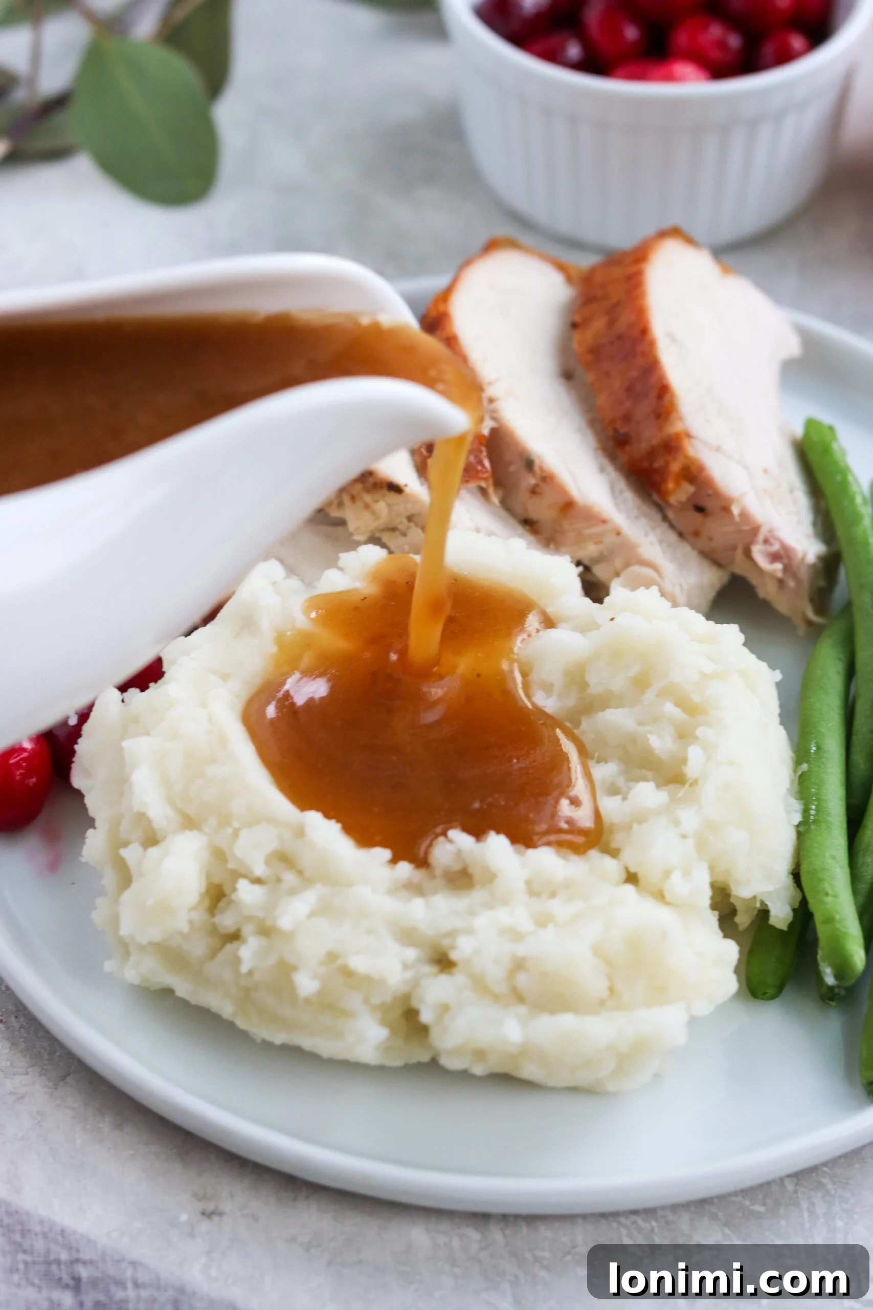 Paleo gravy being generously poured over a serving of creamy dairy-free mashed potatoes with roasted turkey in the background, a perfect holiday meal scene