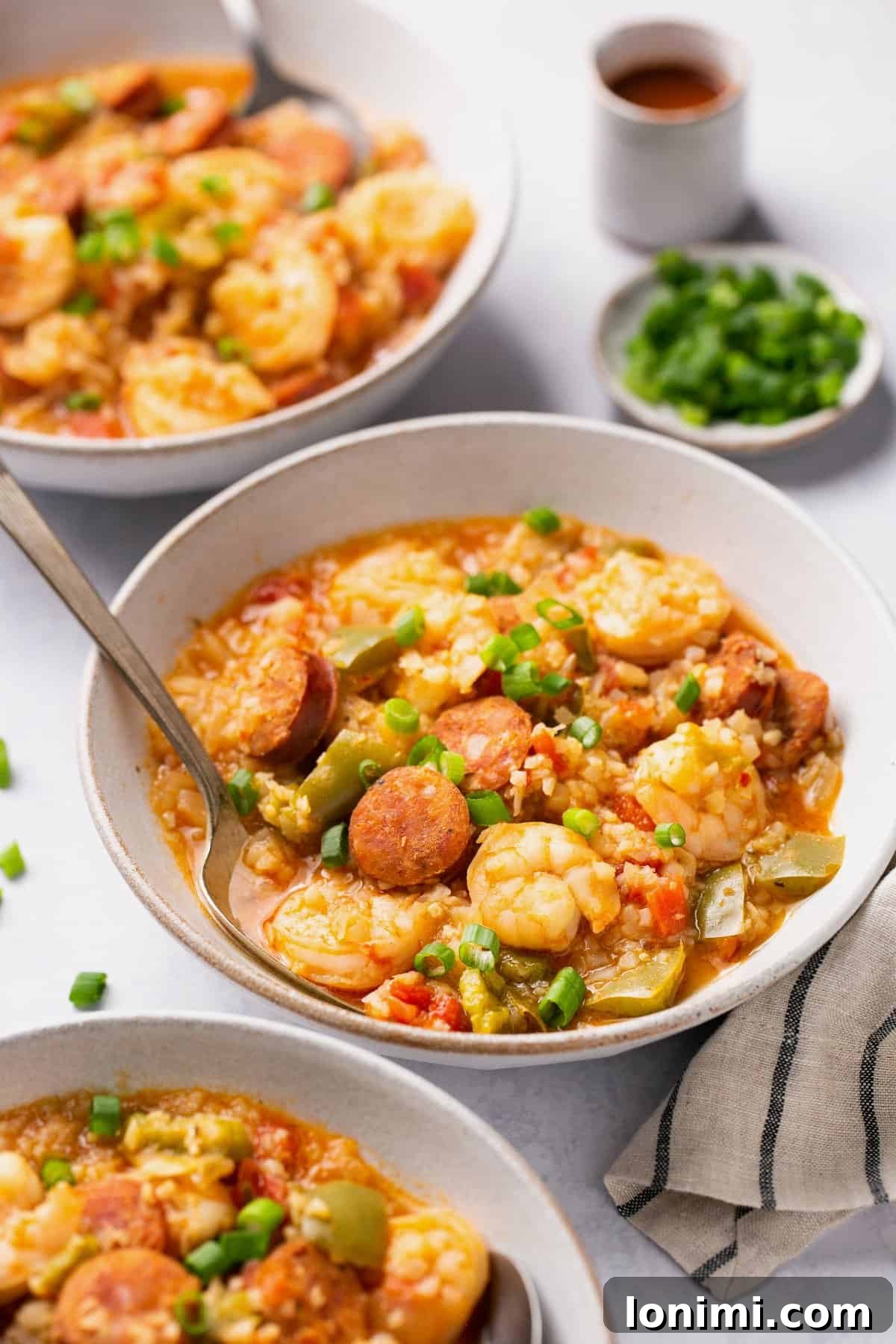 two white bowls of jambalaya topped with scallions 