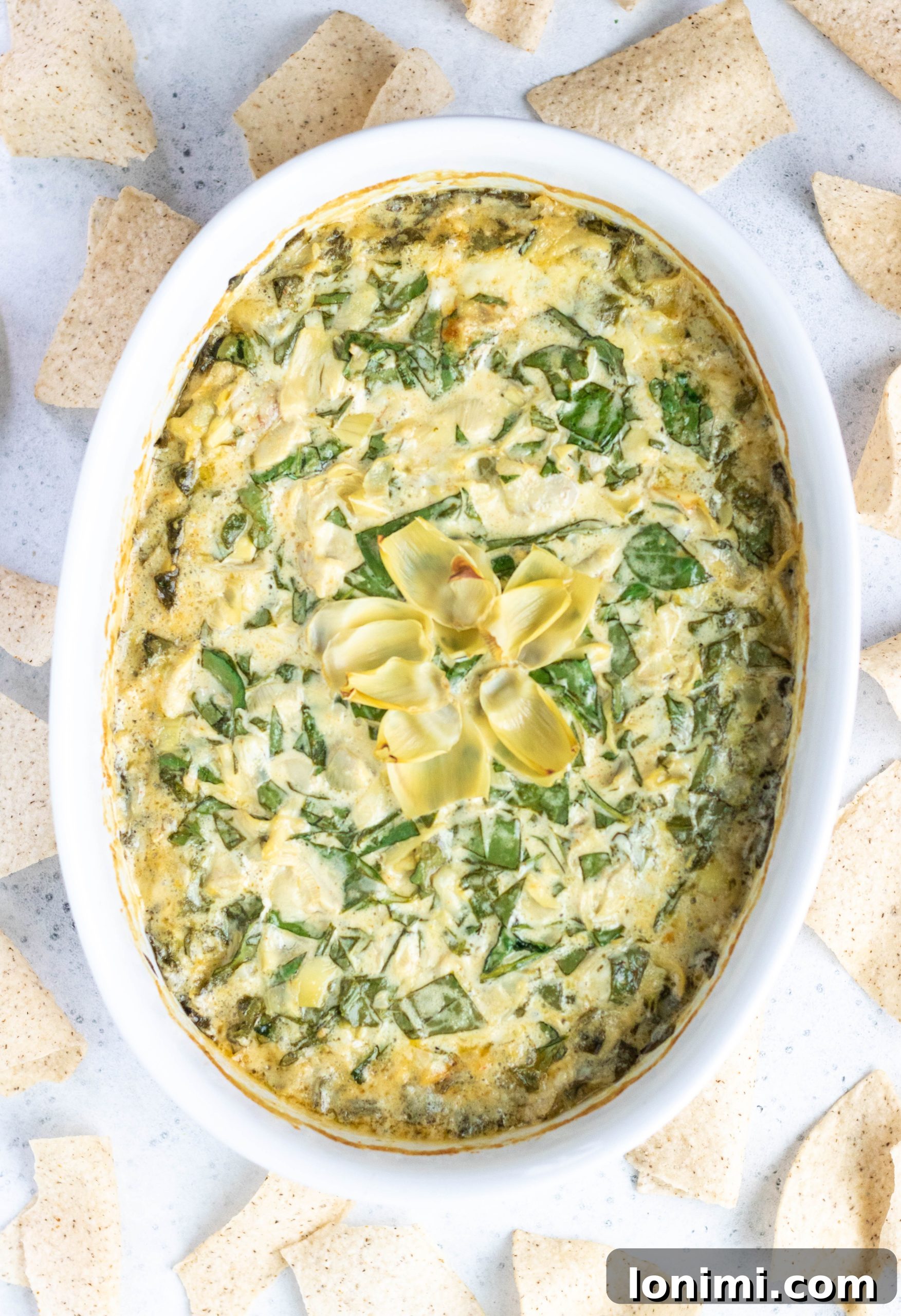 A golden-brown Dairy-Free Spinach Artichoke Dip in a rustic round casserole dish, surrounded by crispy tortilla chips, inviting a delicious scoop.