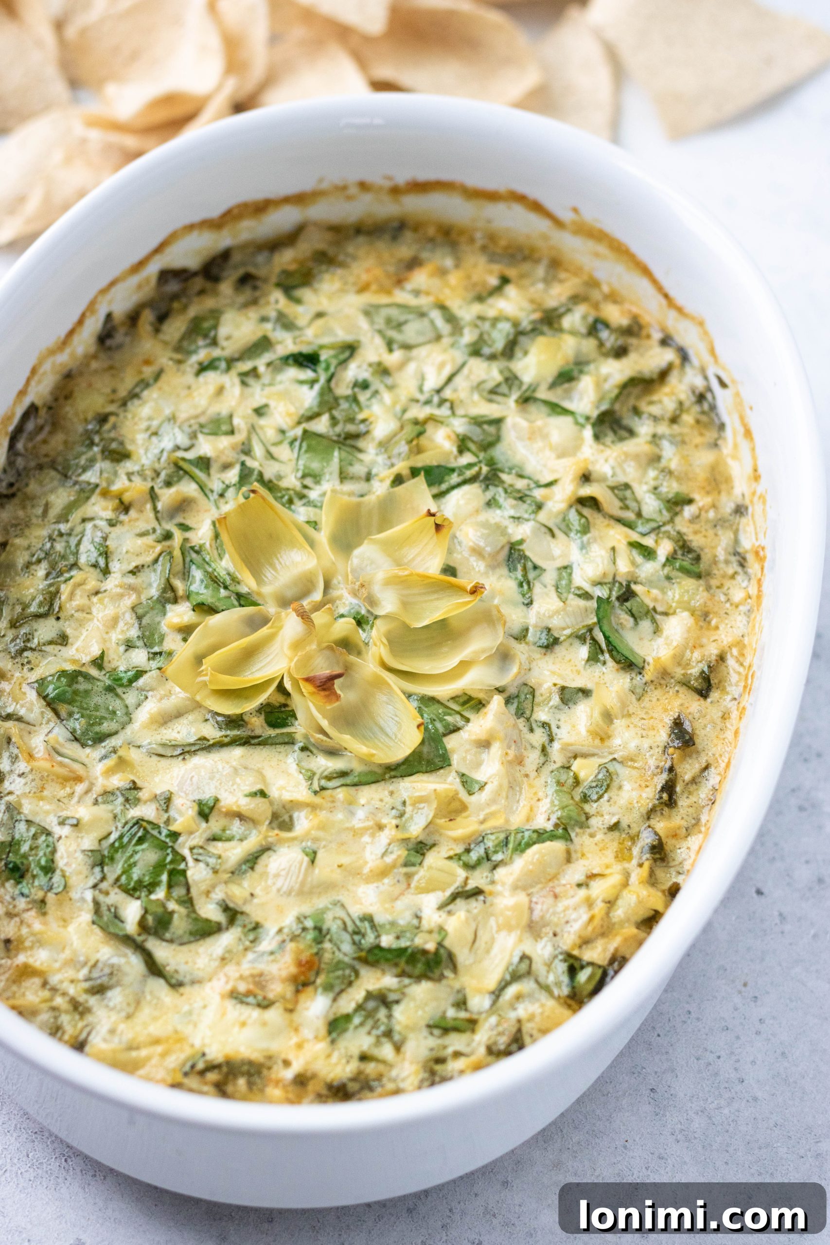 Close-up of a bubbling Dairy-Free Spinach Artichoke Dip in a round baking dish, showcasing its rich and creamy texture.