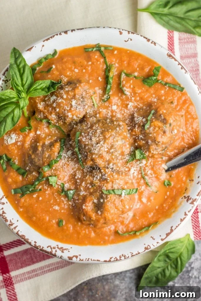 25 Hearty Whole30 Soups, Stews, and Chilis 27 Rich Tomato Basil Bisque served with savory Italian Meatballs, a Paleo and Whole30 comforting meal, garnished with fresh basil.