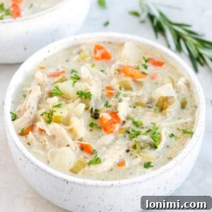 Paleo Chicken Pot Pie Soup with chicken, carrots, celery, and herbs in a white bowl on a gray surface with rosemary