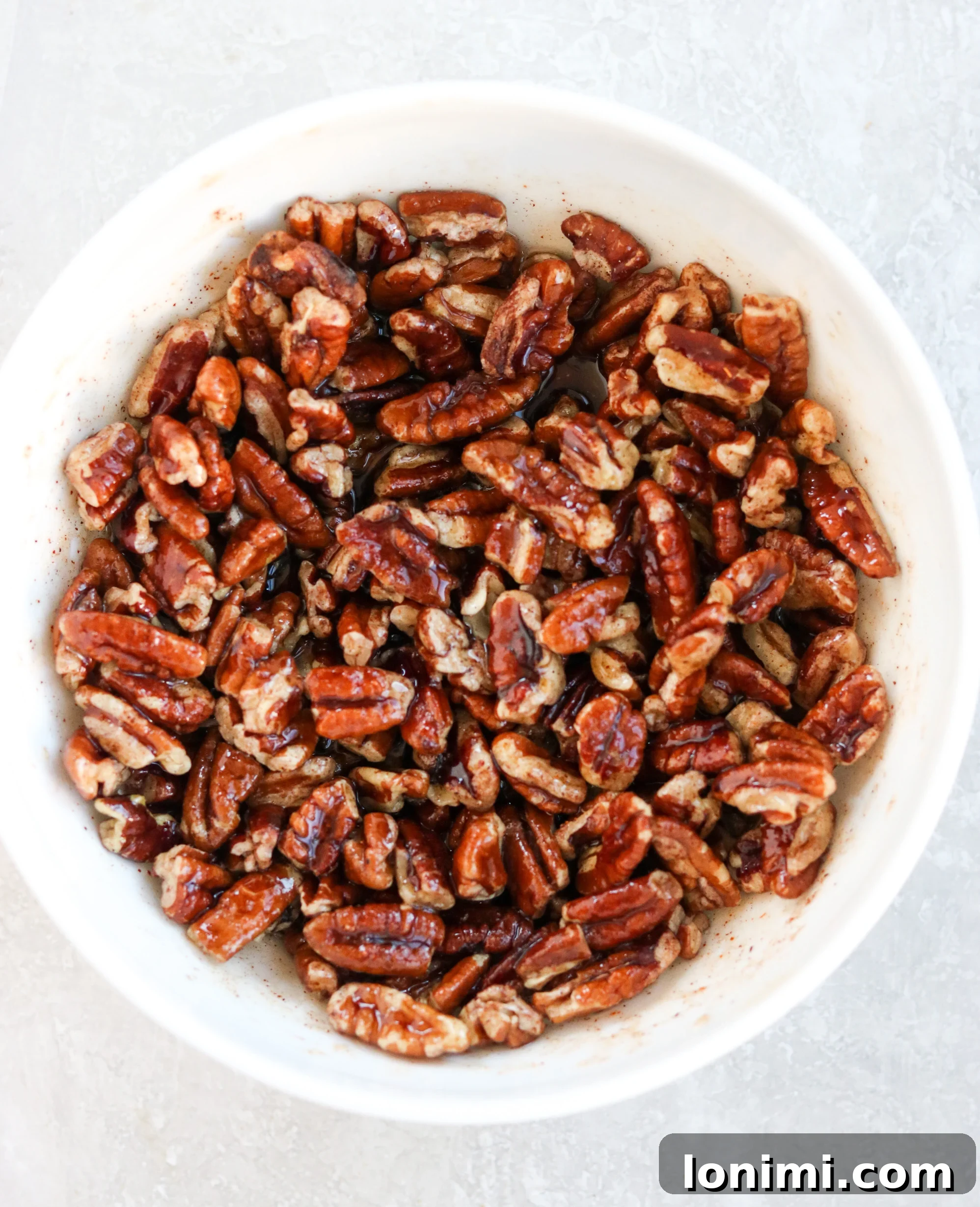 A white bowl filled with the prepared maple cayenne pecan topping, showcasing its crunchy texture and rich color, ready to be spread over the casserole.