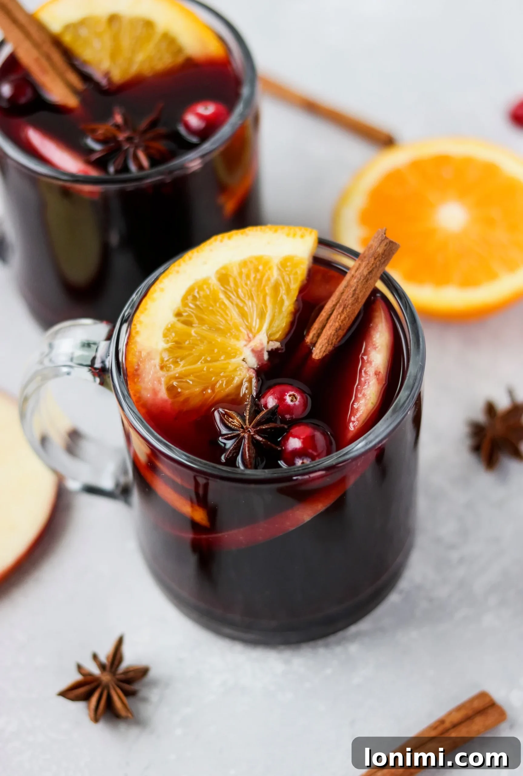 Mulled wine in a cozy mug, garnished with orange and cinnamon, with a festive background.