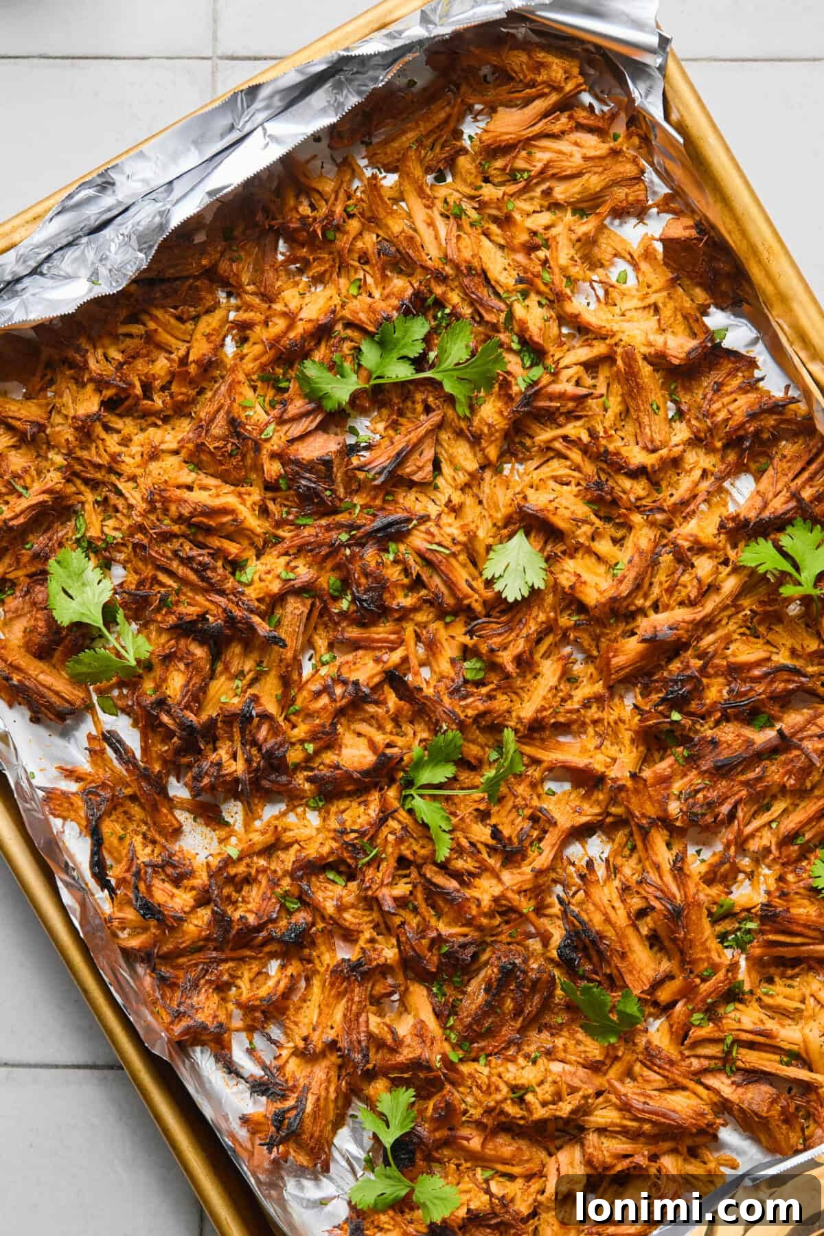 Crispy shredded pork carnitas garnished with fresh cilantro on a foil-lined baking sheet, ready to serve.
