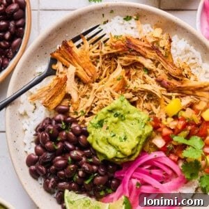 slow cooker carnitas in a bowl with rice, pickled onions, black beans, mango salsa and guacamole