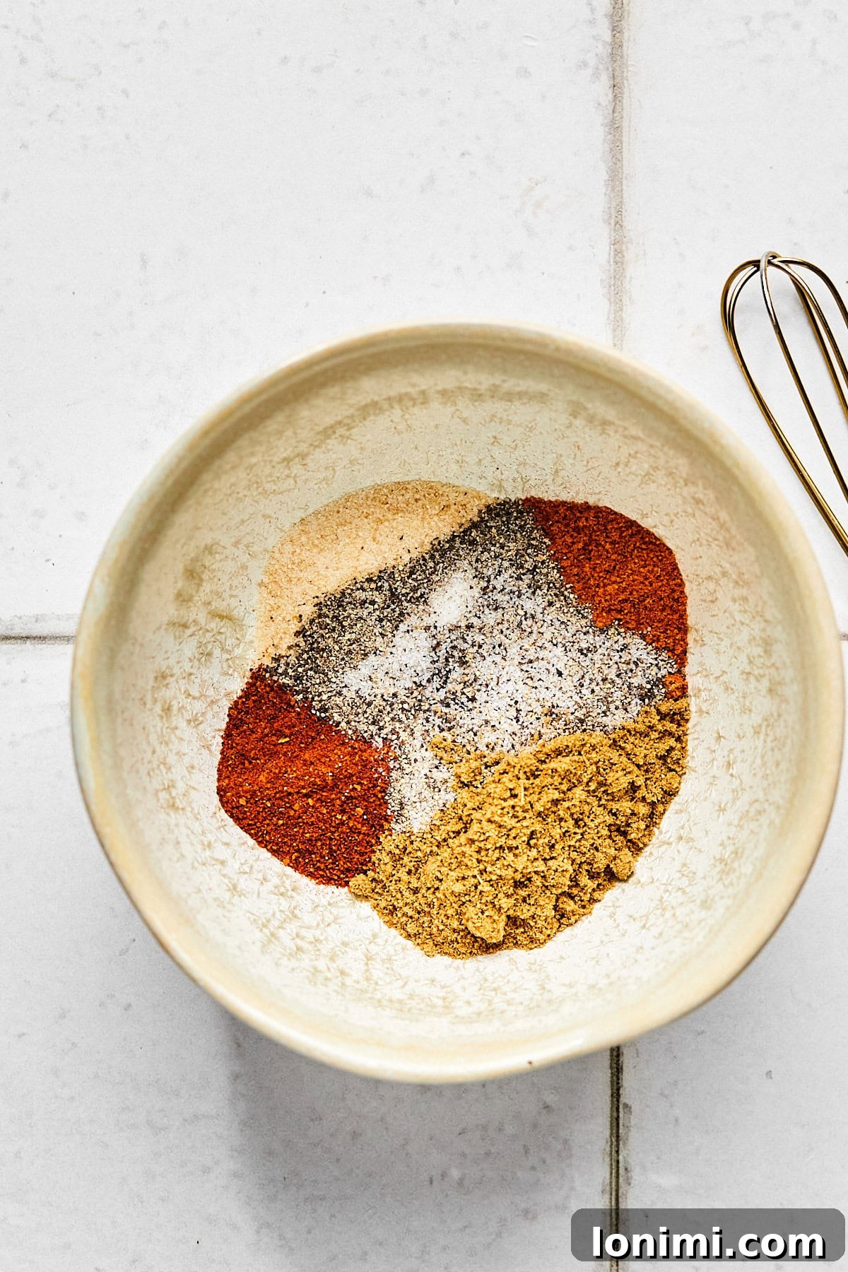 A small white bowl filled with a vibrant spice rub mixture, featuring cumin, chili powder, and cayenne pepper, ready to be applied to pork.