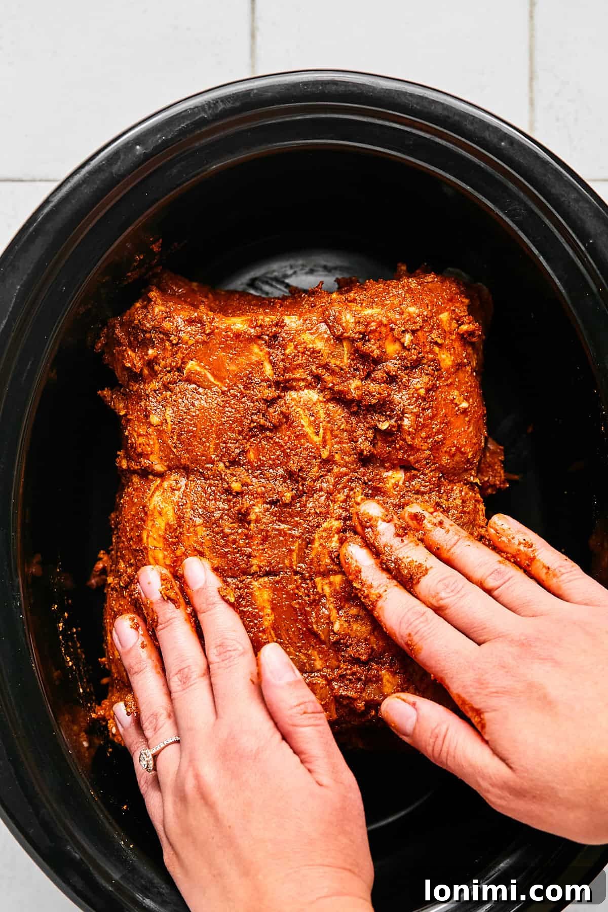 A raw pork roast seasoned generously with a spice rub, placed inside a slow cooker, ready for cooking.