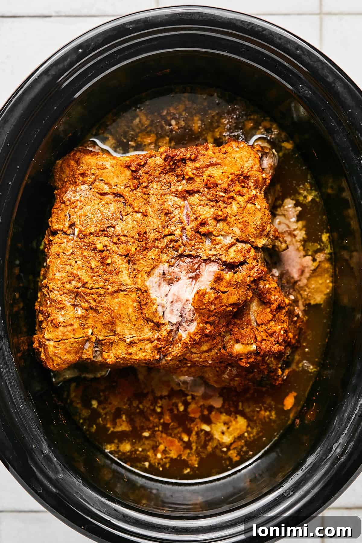 A close-up view of the pork roast cooking in the slow cooker, surrounded by citrus juice, minced garlic, and chicken broth, bubbling gently.