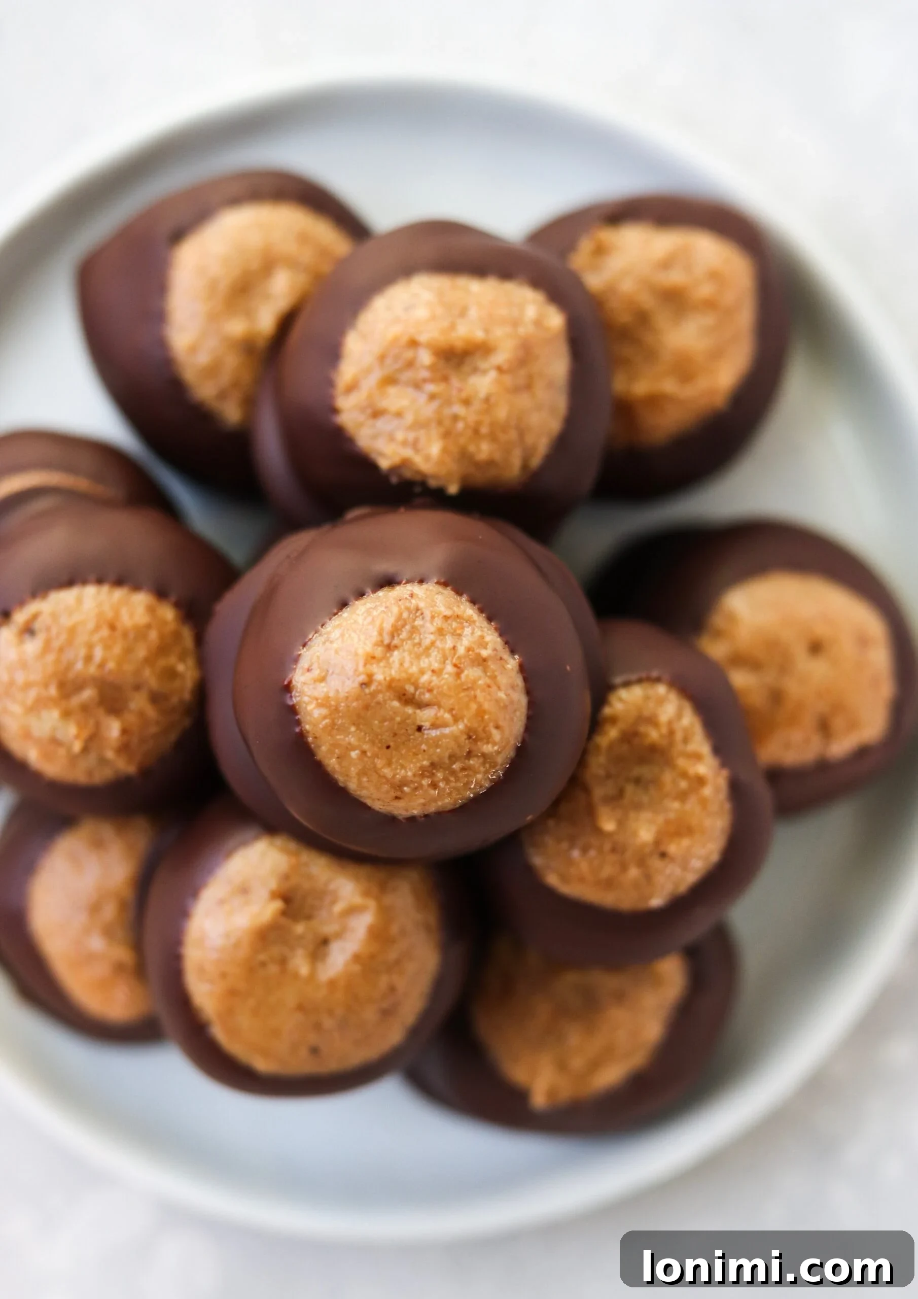 A close-up of a Paleo Buckeye Ball, showing the perfectly smooth dark chocolate coating and a glimpse of the rich, creamy filling.