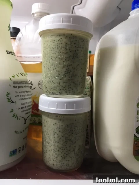 Overhead shot of a mason jar filled with green matcha chia pudding, adorned with a wooden spoon and various fresh toppings like berries and nuts spread around it on a rustic surface.