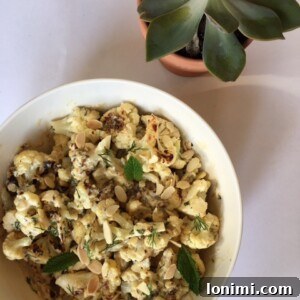 A beautifully presented bowl of Roasted Cauliflower with Tahini, garnished with fresh herbs and almonds.