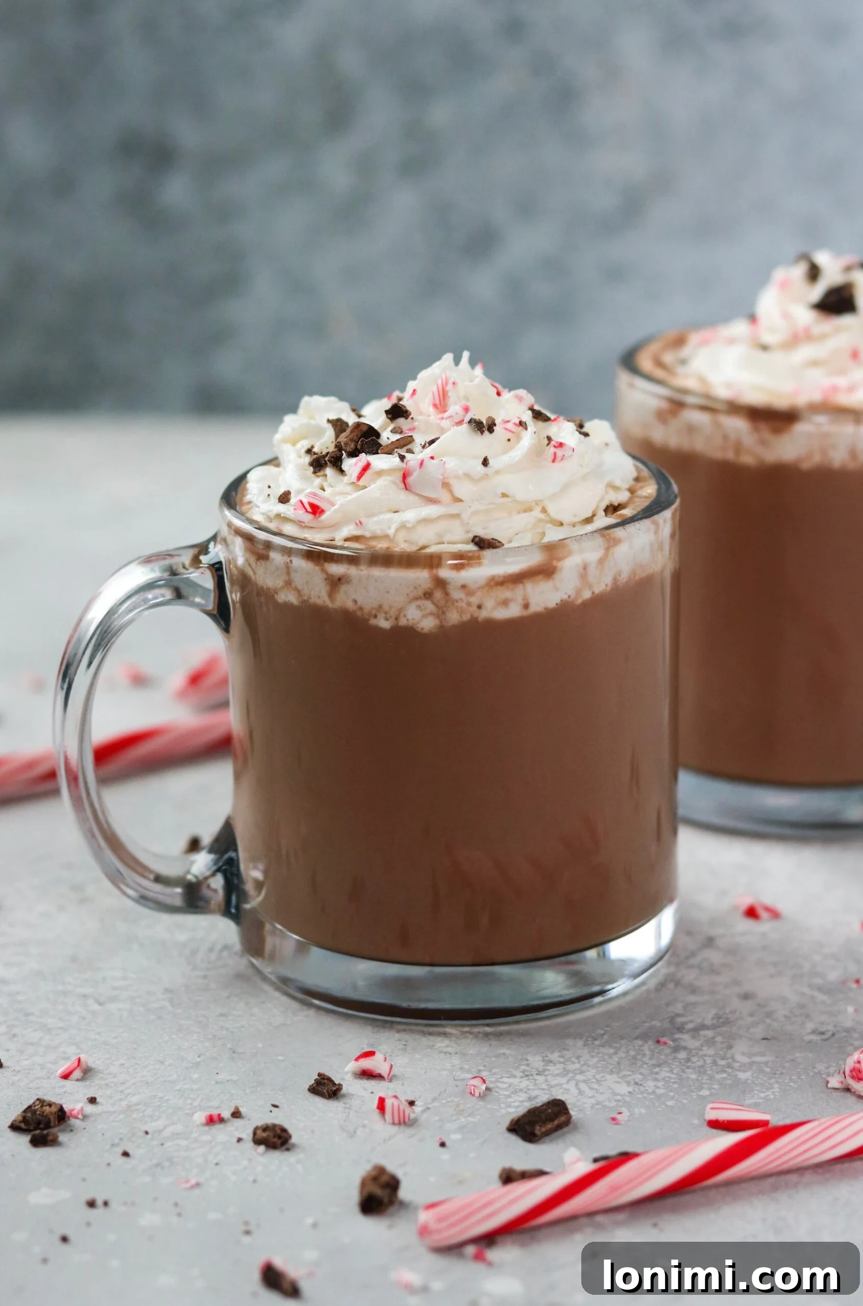 Hearthside Holiday Cocoa 2 A close-up of a glass mug filled with creamy, dairy-free Christmas hot chocolate, generously topped with fluffy coconut whipped cream and festive peppermint shavings, inviting you to take a sip.