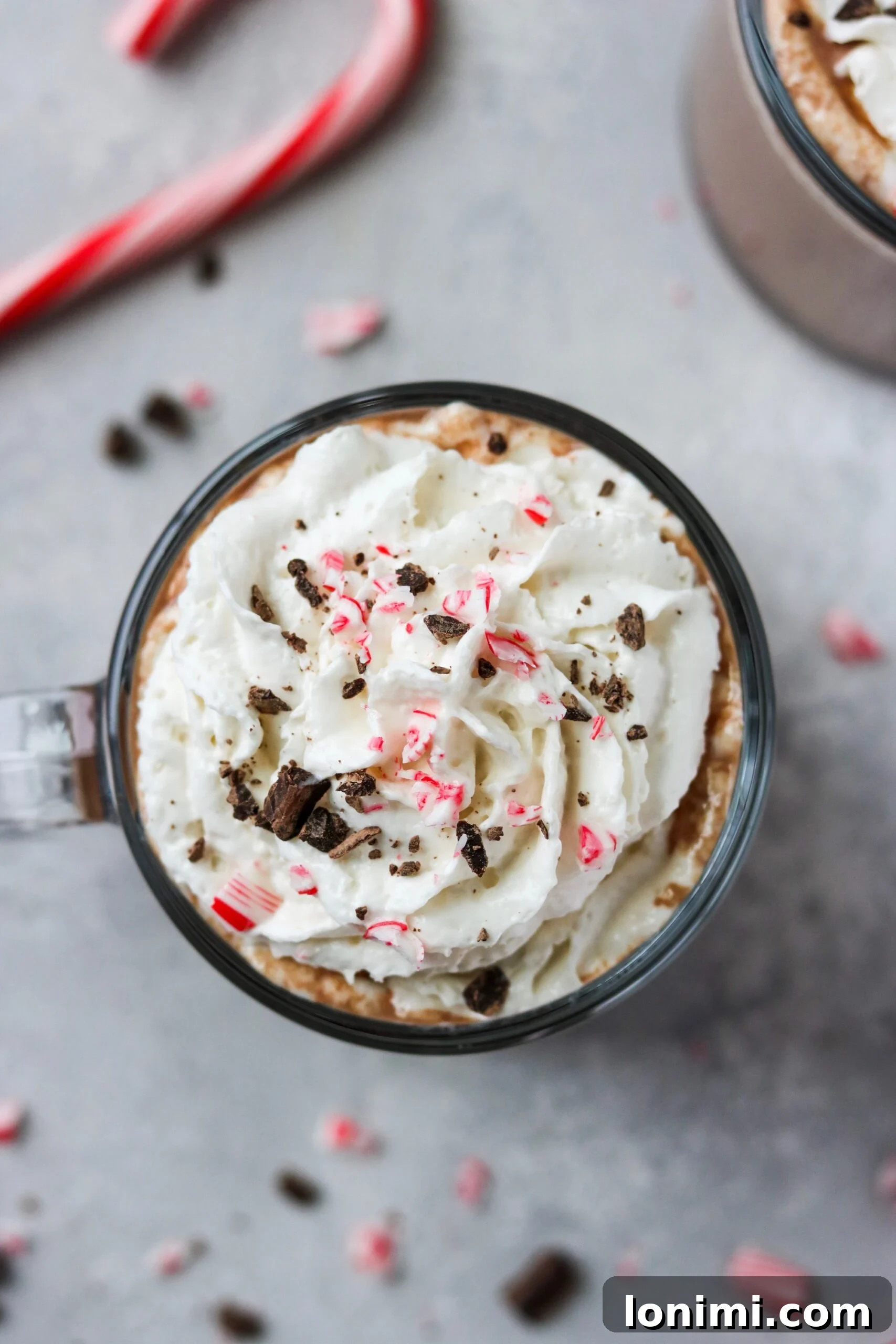 Hearthside Holiday Cocoa 3 An inviting overhead view of a mug of Christmas hot chocolate, artfully garnished with a swirl of whipped cream, festive peppermint fragments, and delicate chocolate crumbles, promising a delightful treat.