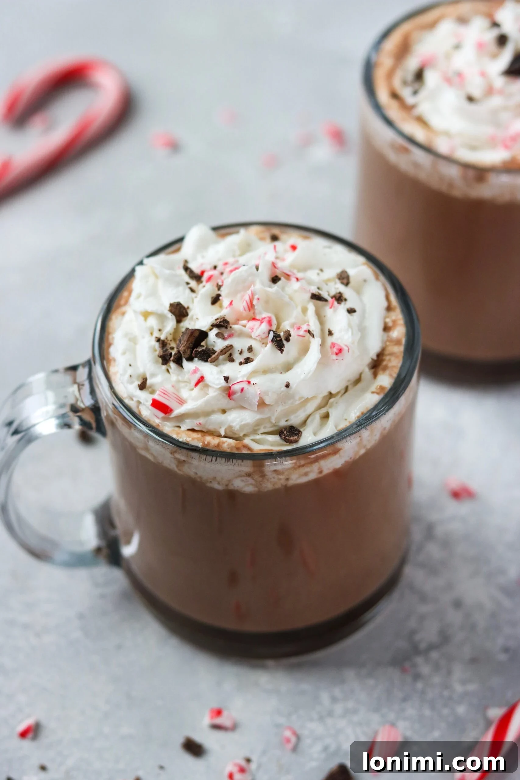 Hearthside Holiday Cocoa 4 A charming side view of a glass mug filled with Christmas hot chocolate, artfully topped with whipped cream and a candy cane, evoking a sense of festive cheer.