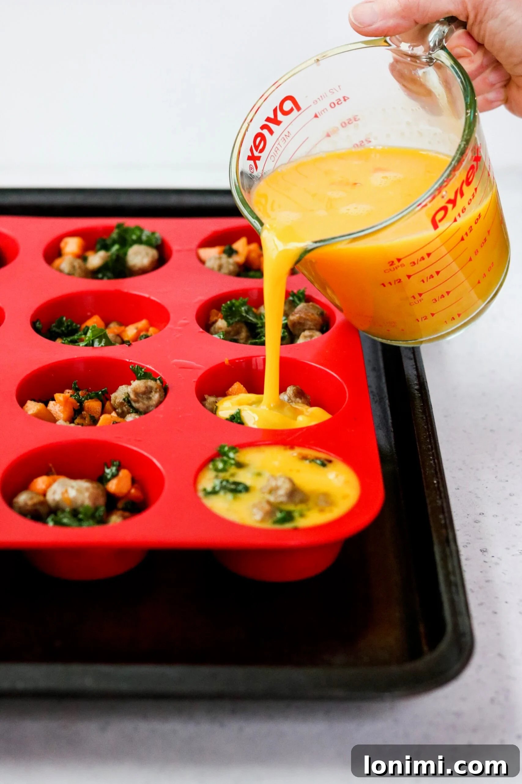 Unbaked sausage, sweet potato, and kale egg cups in a silicone muffin pan
