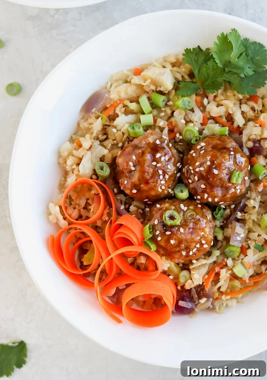 Delicious Asian Pork Meatball Bowls with a sticky glaze and cauliflower fried rice, garnished with green onions and sesame seeds.
