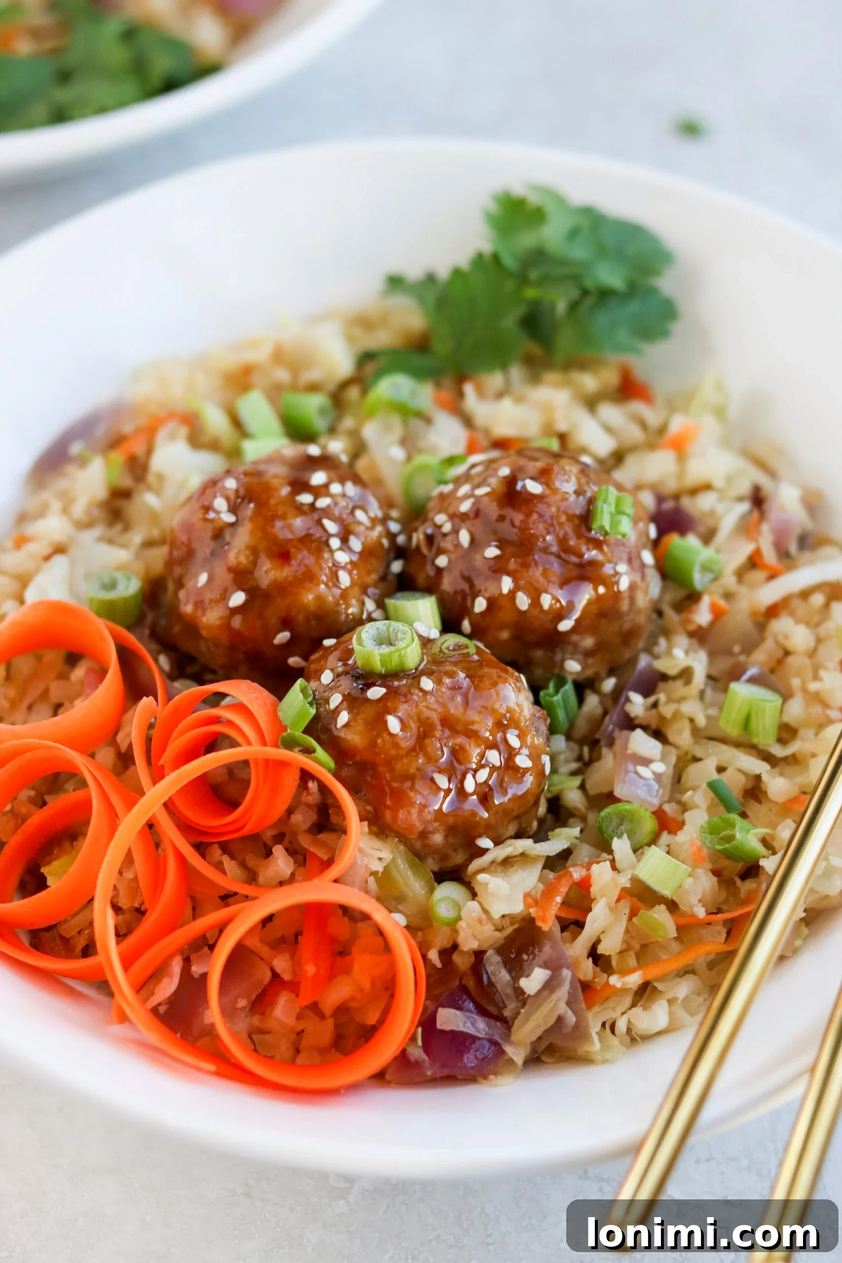 Close-up of a single Asian pork meatball on a fork, showing the sticky glaze and texture, with a blurred background of the meal.